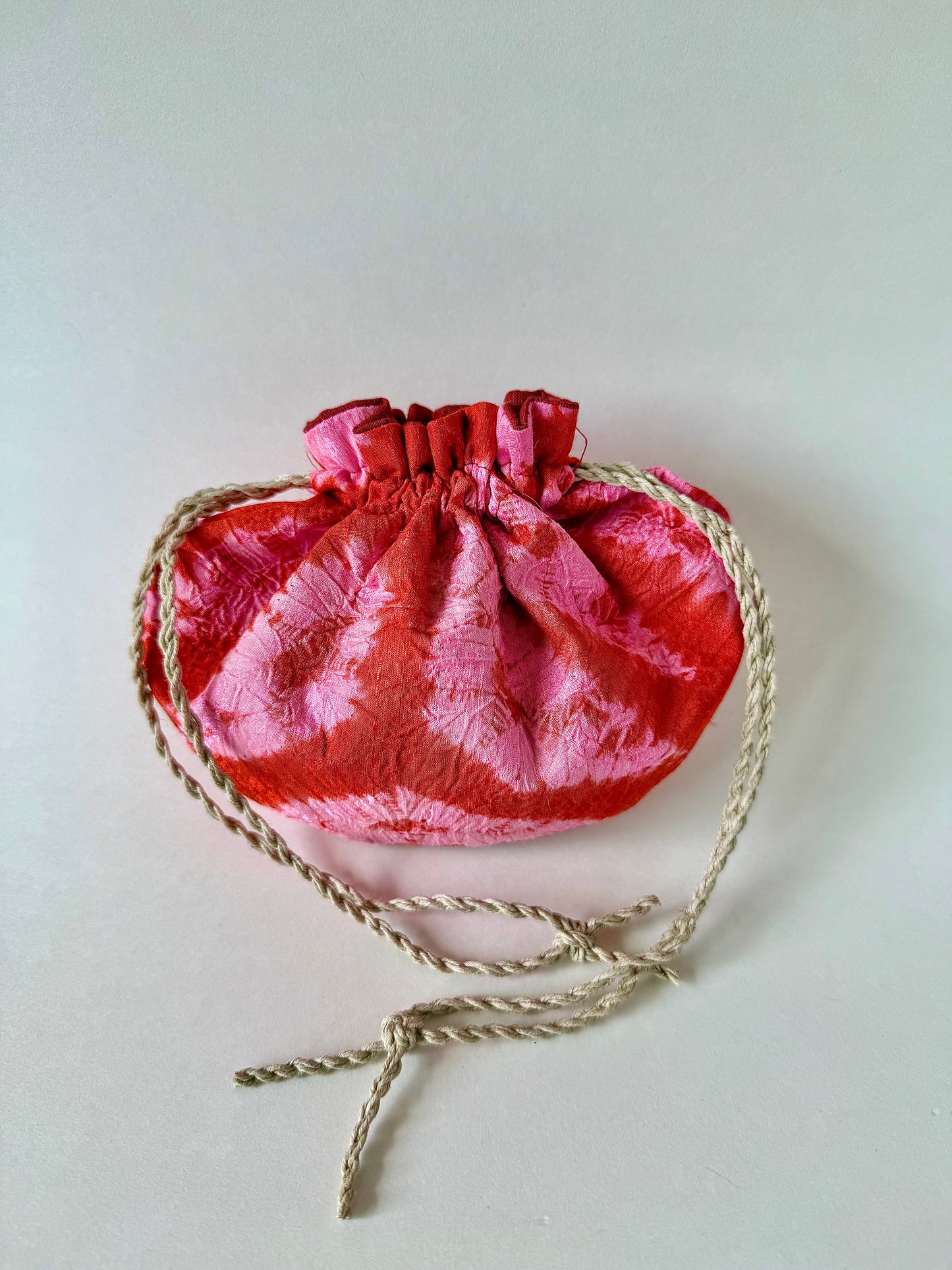 Backside of cinched hemp drawstrings on pink and red kimono silk pouch