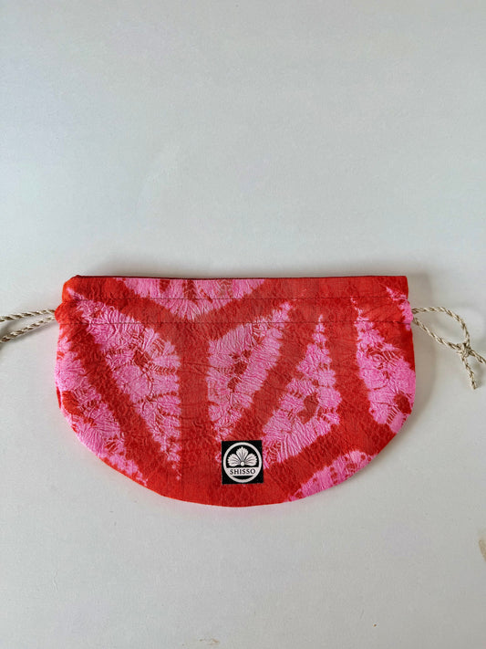 Front view of flay laying red and pink kimon fabric drawstring bag with sheen accents