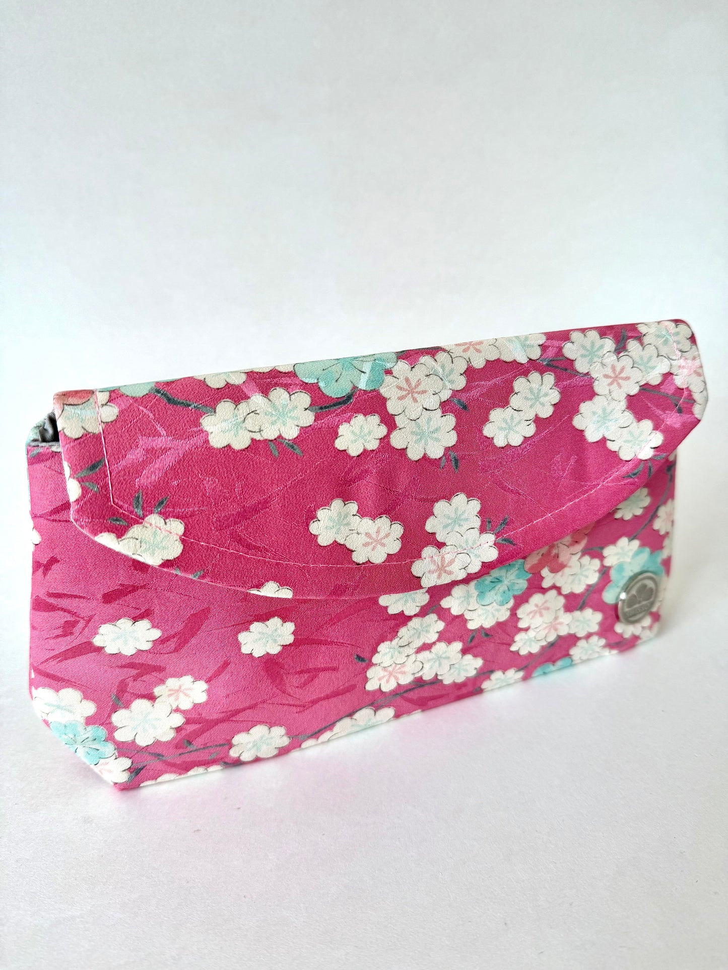 Angled view of pink kimono silk clutch showing subtle brushstroke pattern and fold-over design