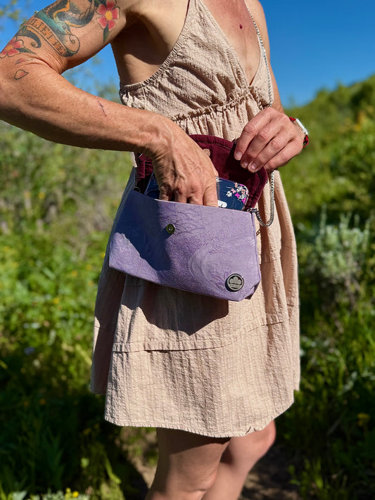 Phone being removed from purple clutch bag made from 1960s Chirimen kimono silk with traditional Japanese wave and floral motifs.