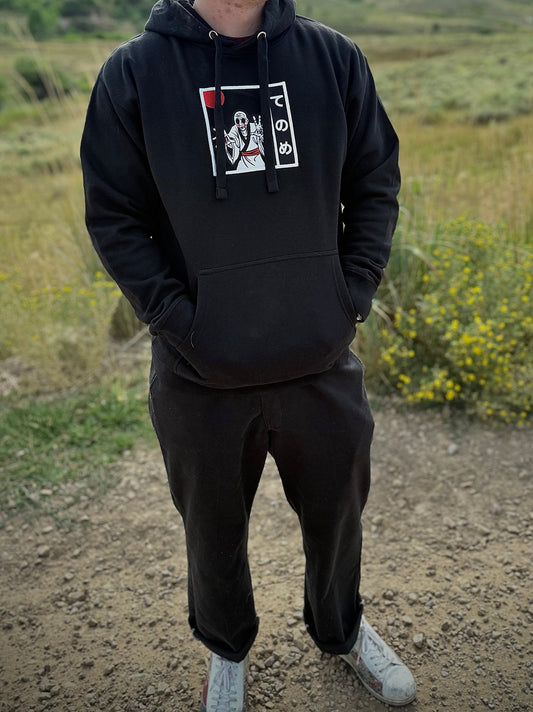 Person wearing black streetwear hoodie with embroidered Tenome yokai, with hands in front hoodie pocket.