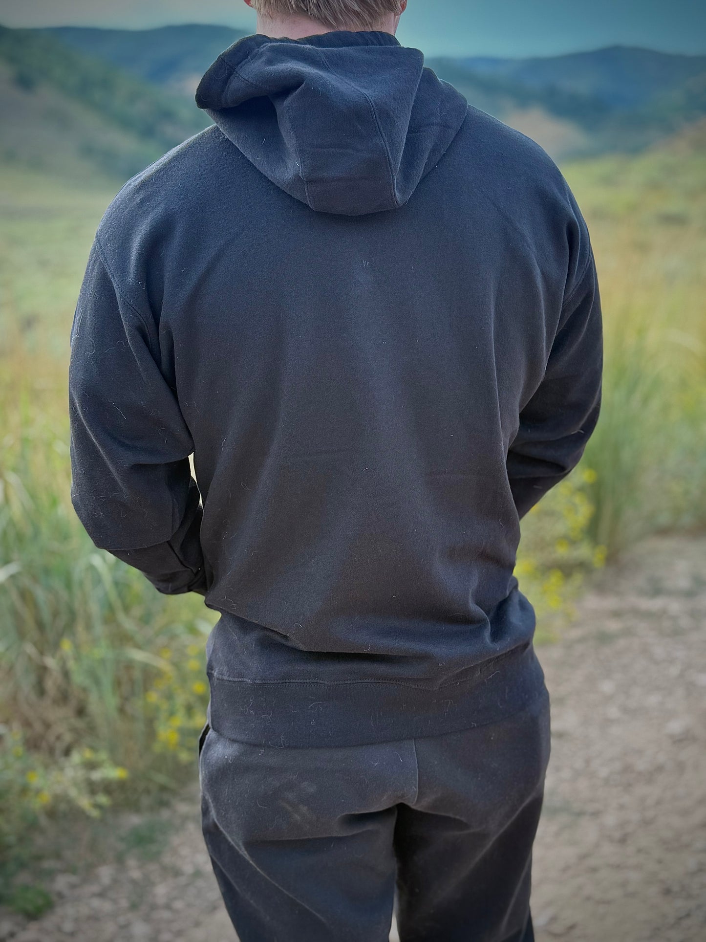 Back view of model wearing black Japanese design yokai hoodie in nature background, showing plain black fabric and clean minimalist design.