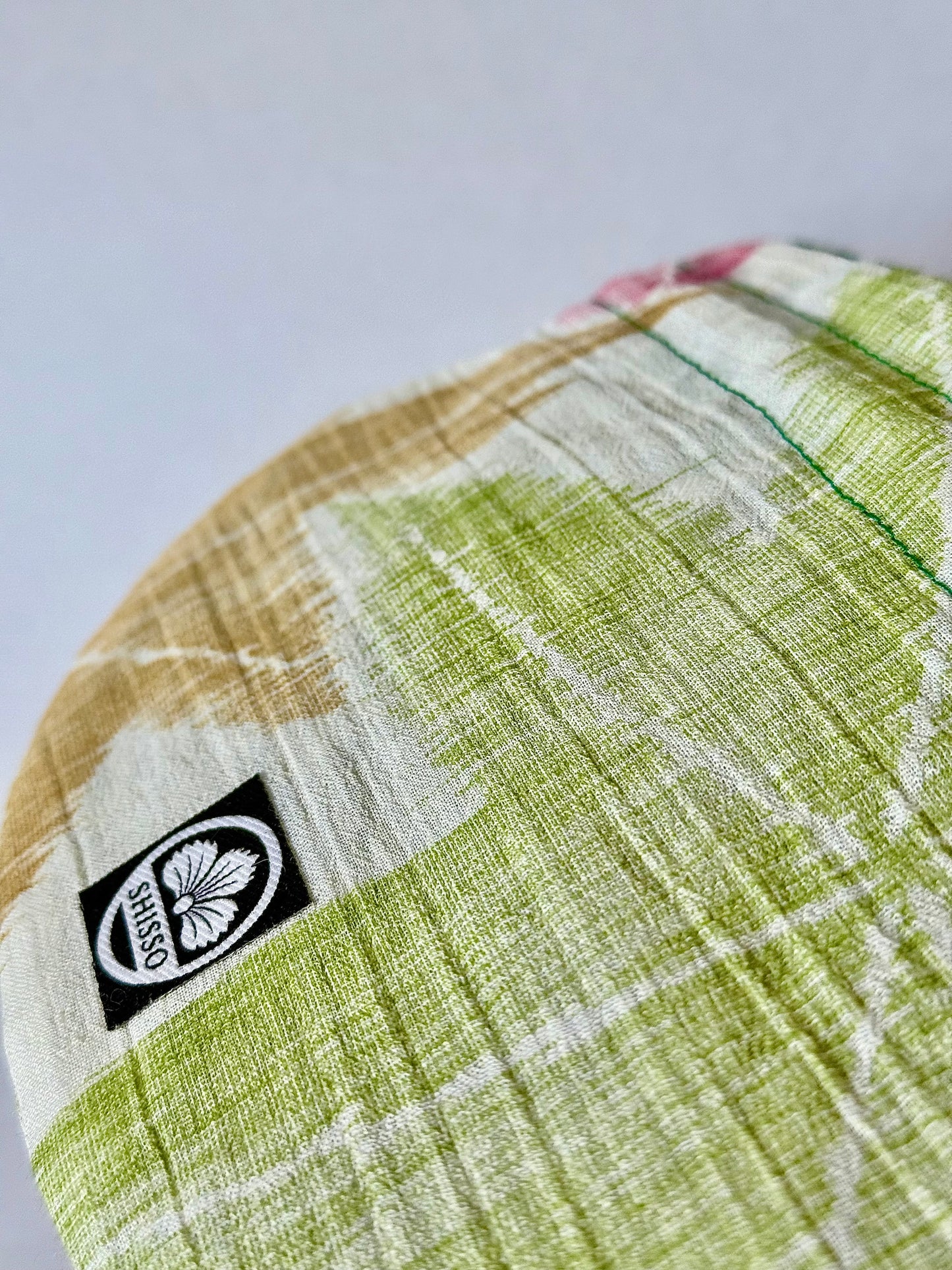 Close up of woven texture of off white kimono silk drawstring pouch with green, yellow, and red maple leaf patterns