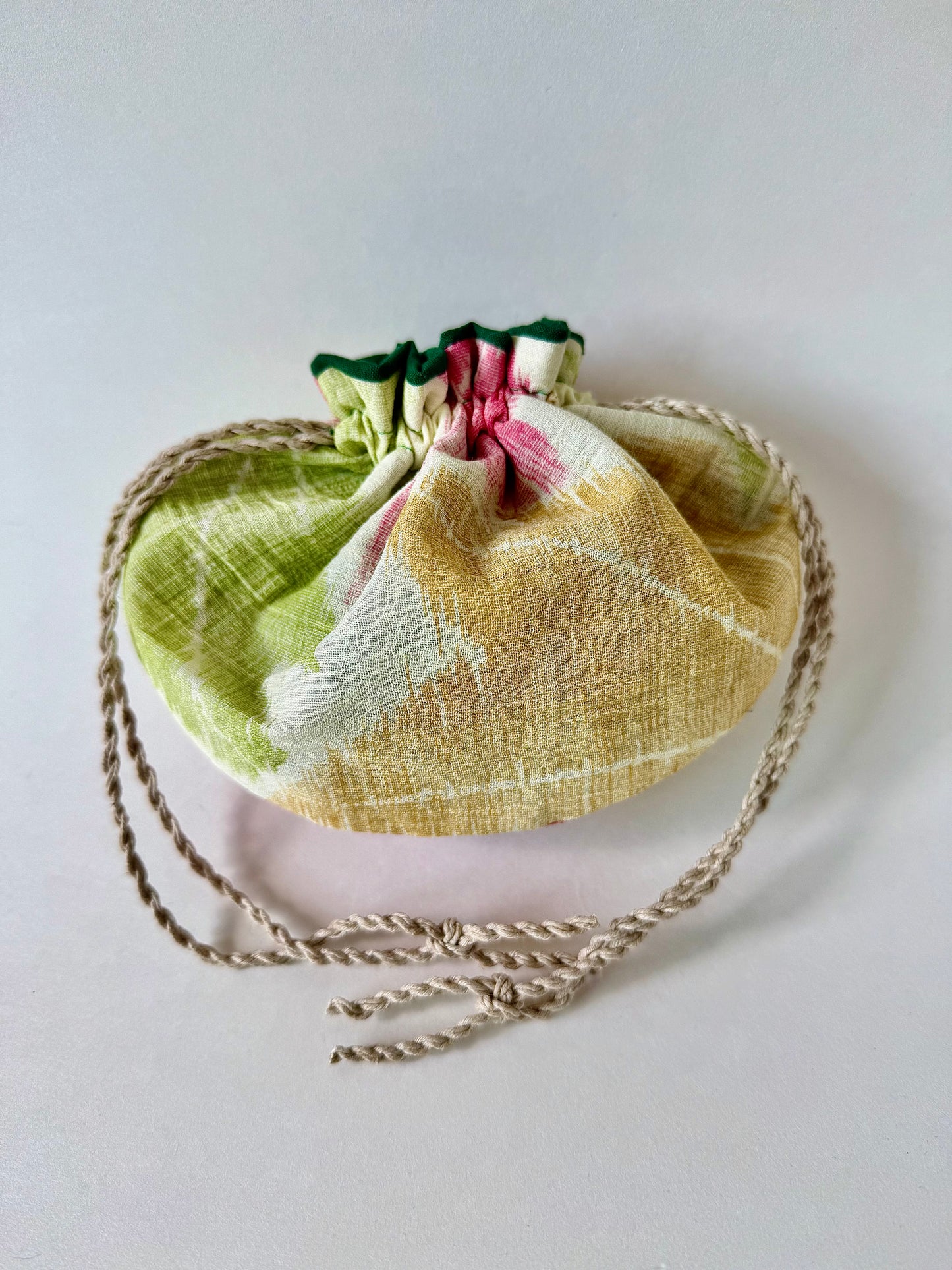 Back view of cinched closed beige kimono sha silk pouch featuring red, green, and yellow momiji motifs and natural hemp drawstrings