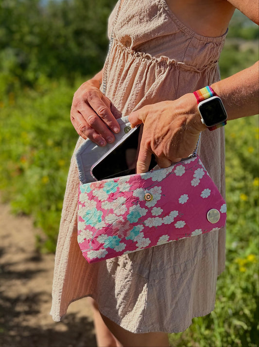 Hand taking phone out of handmade pink clutch bag crafted from 1960s vintage kimono silk with sakura design.