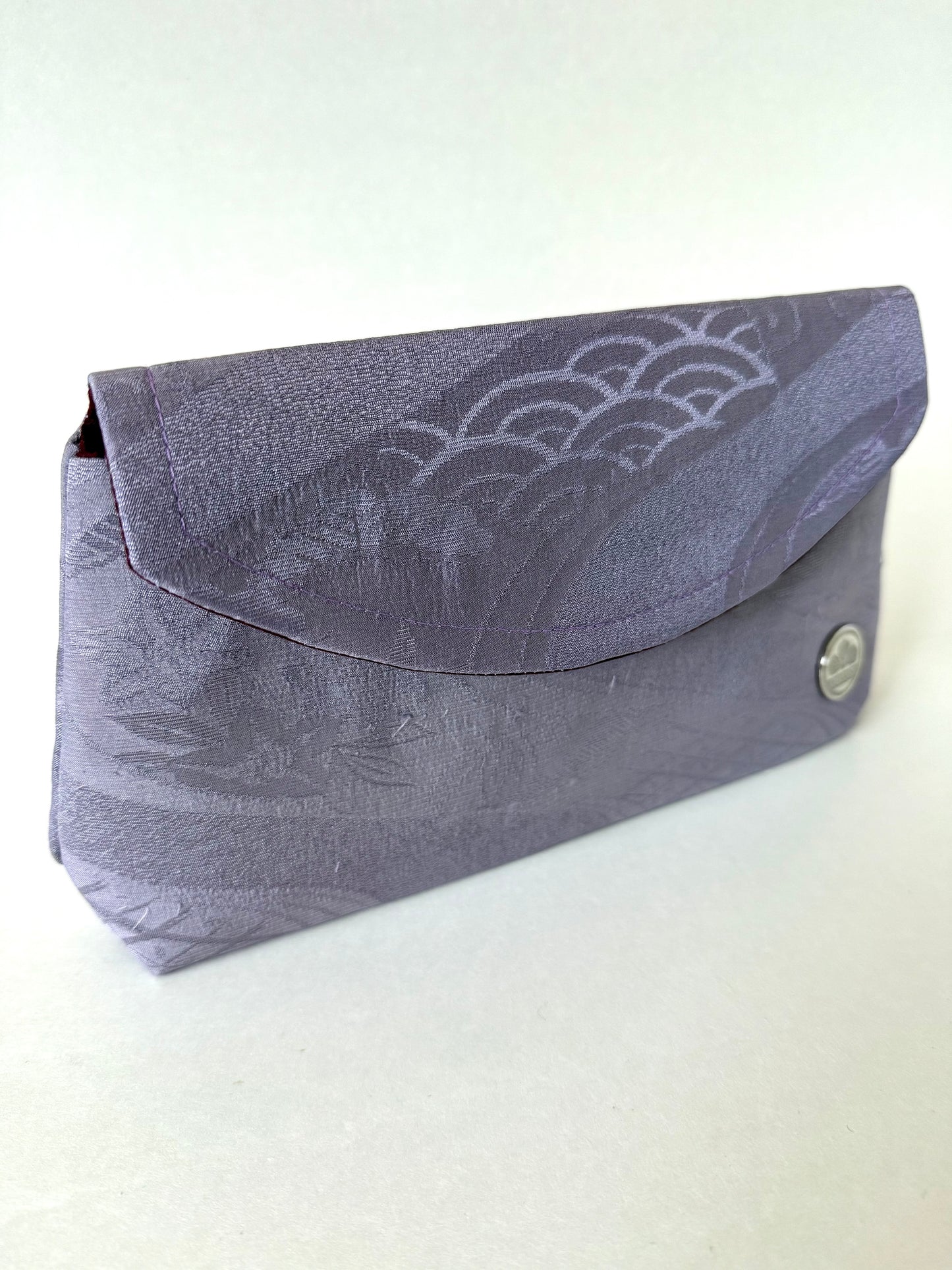 Front left angle view of purple kimono silk clutch bag with varying motifs including seigaiha prominently on the front