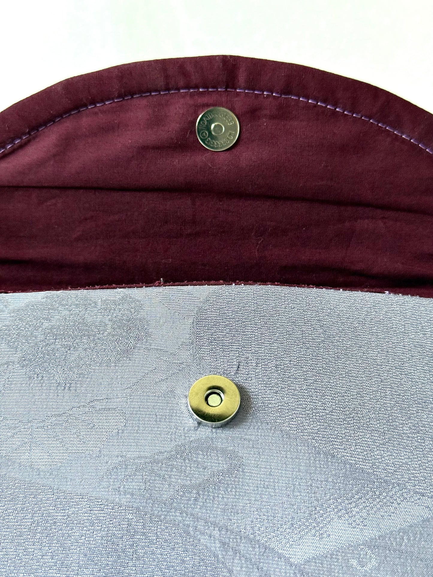 Close up of metal magnetic closure on purple kimono silk fold-over clutch