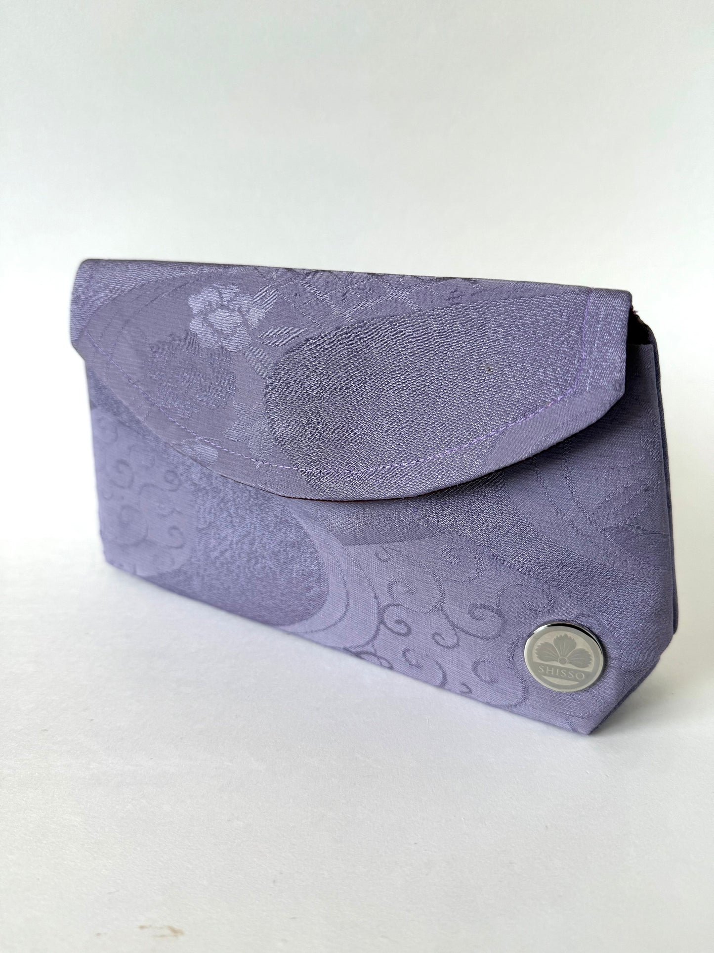 Front angled view of purple, crepe textured kimono silk fold-over clutch with floral and flowing water motifs