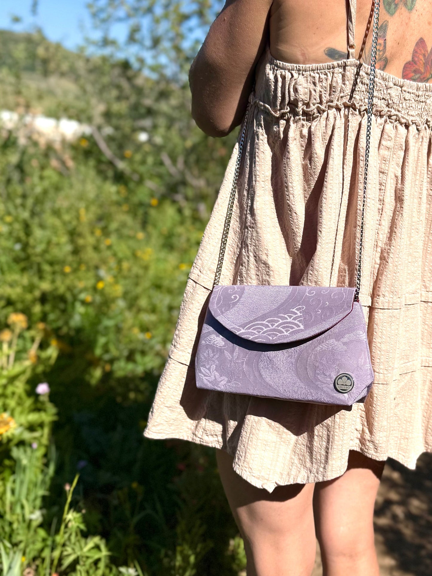 Fold-over purple kimono chirimen silk clutch bag carried with metal chain strap over the shoulder outdoors