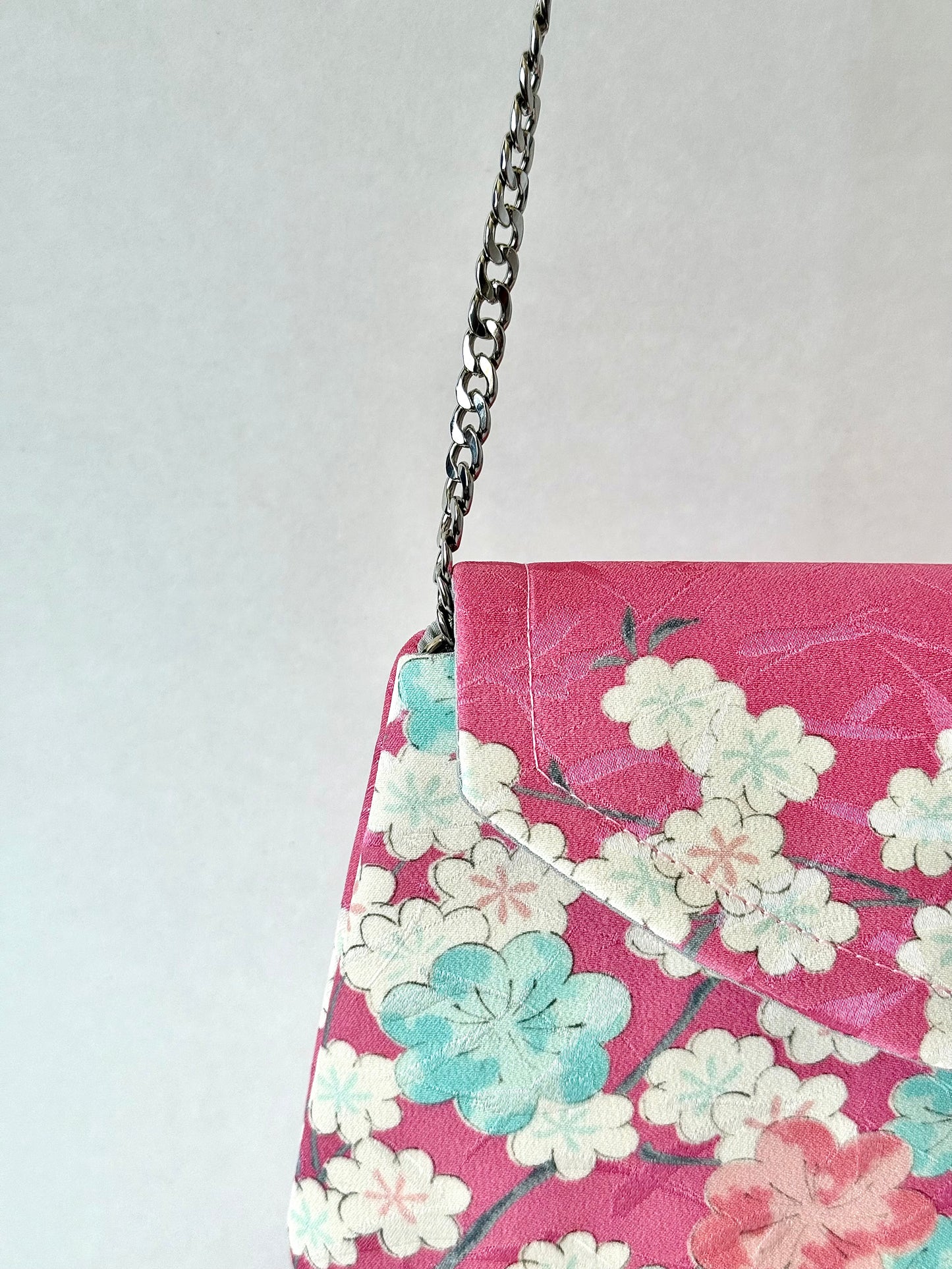 Silver colored metal chain strap on pink clutch bag with sakura motif