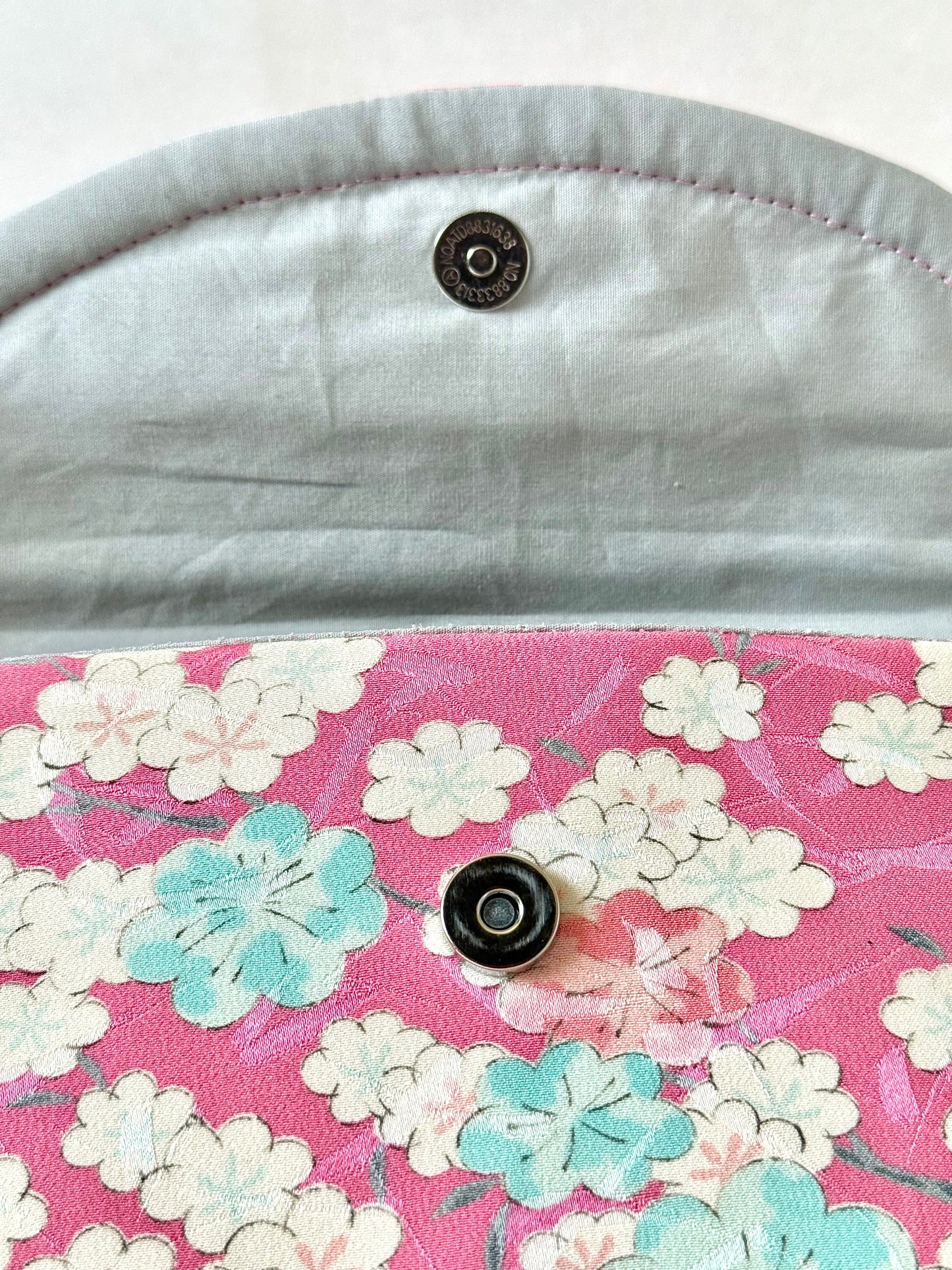 Silver colored magnetic closure on foldover clutch bag with cherry blossom flower motif