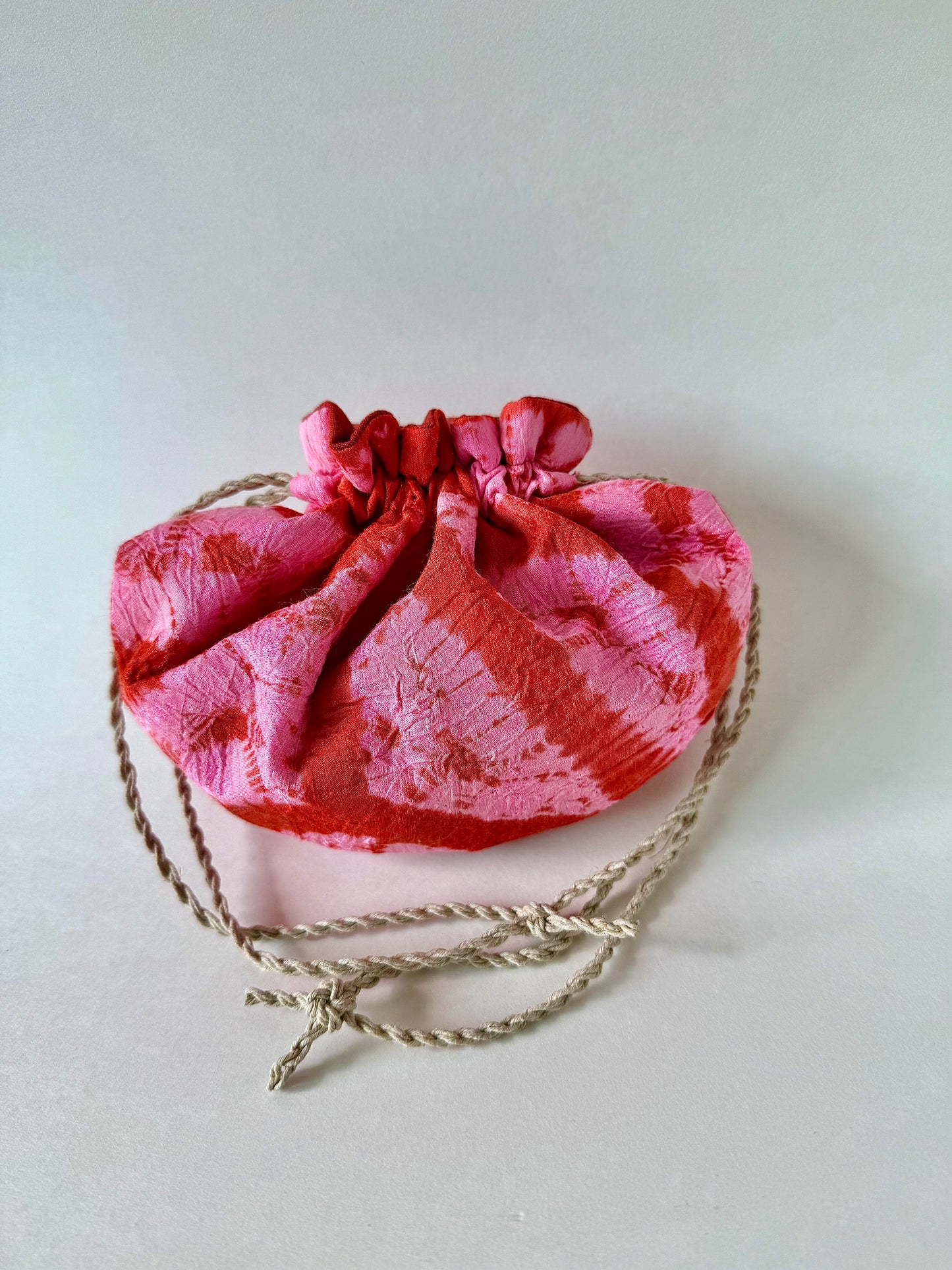 Back view of cinched red and pink shibori silk drawstring bag with natural hemp drawstrings