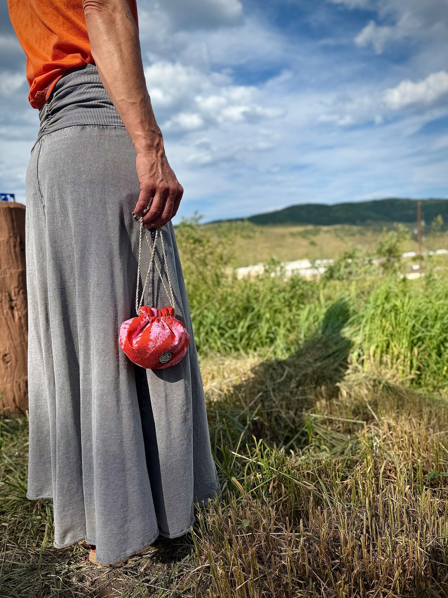 Red and pink kimono silk drawstring pouch being carried in the hand by natural hemp drawstrings in nature