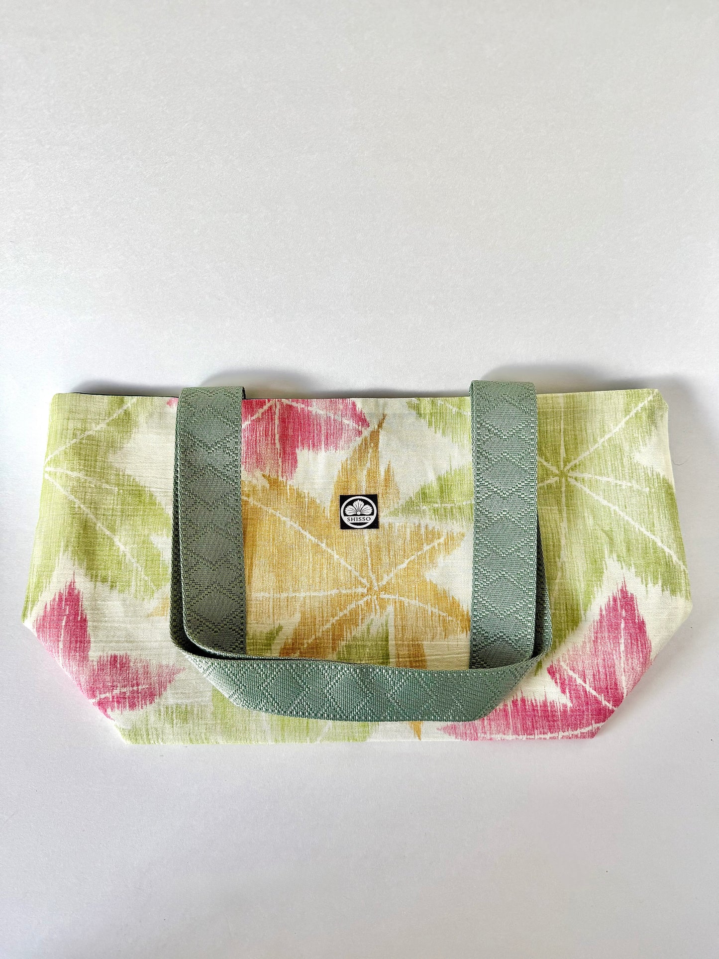 Kimono silk tote bag with maple leaf motifs laying flat with green handles folded on top