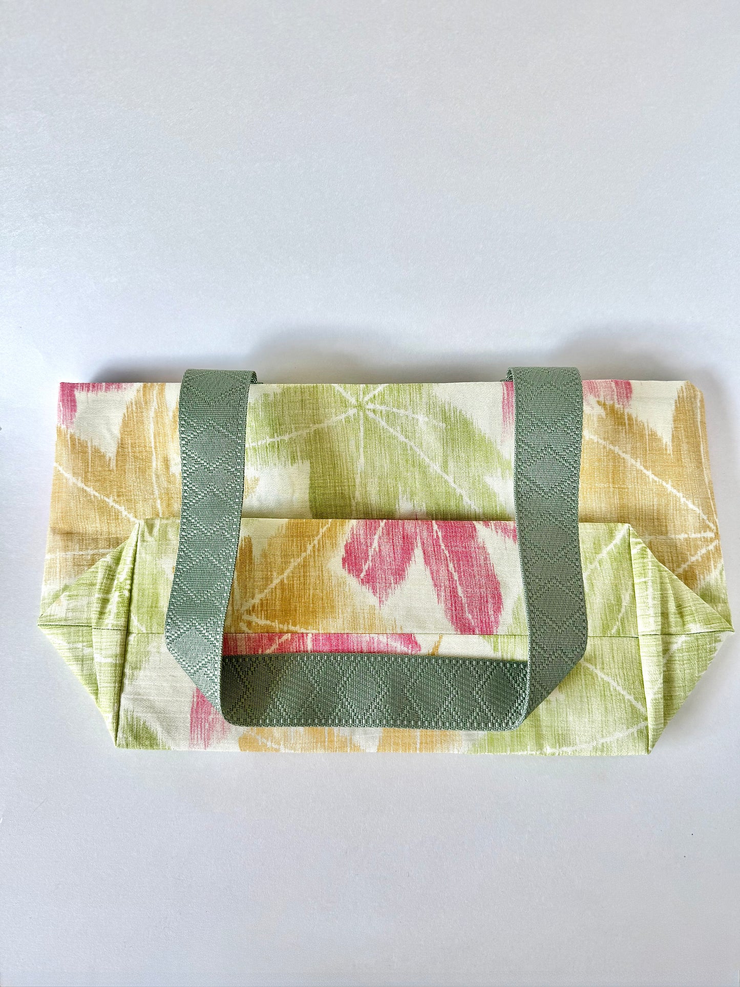 Backside of flat laying kimono silk tote bag with dark green handle folded on top
