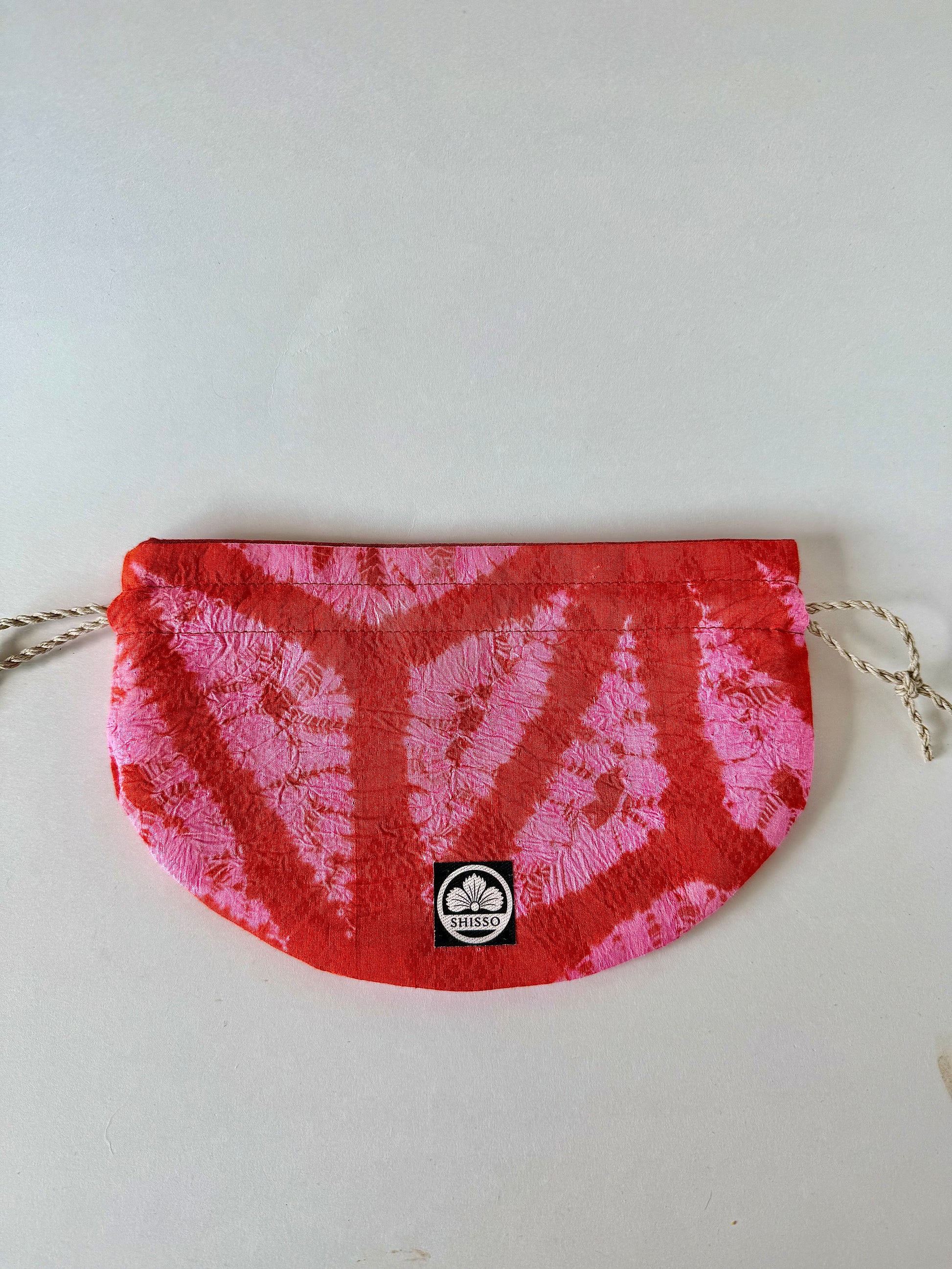 Front view of flay laying red and pink kimon fabric drawstring bag with sheen accents