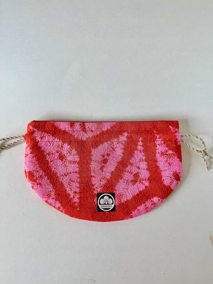Front view of flay laying red and pink kimon fabric drawstring bag with sheen accents
