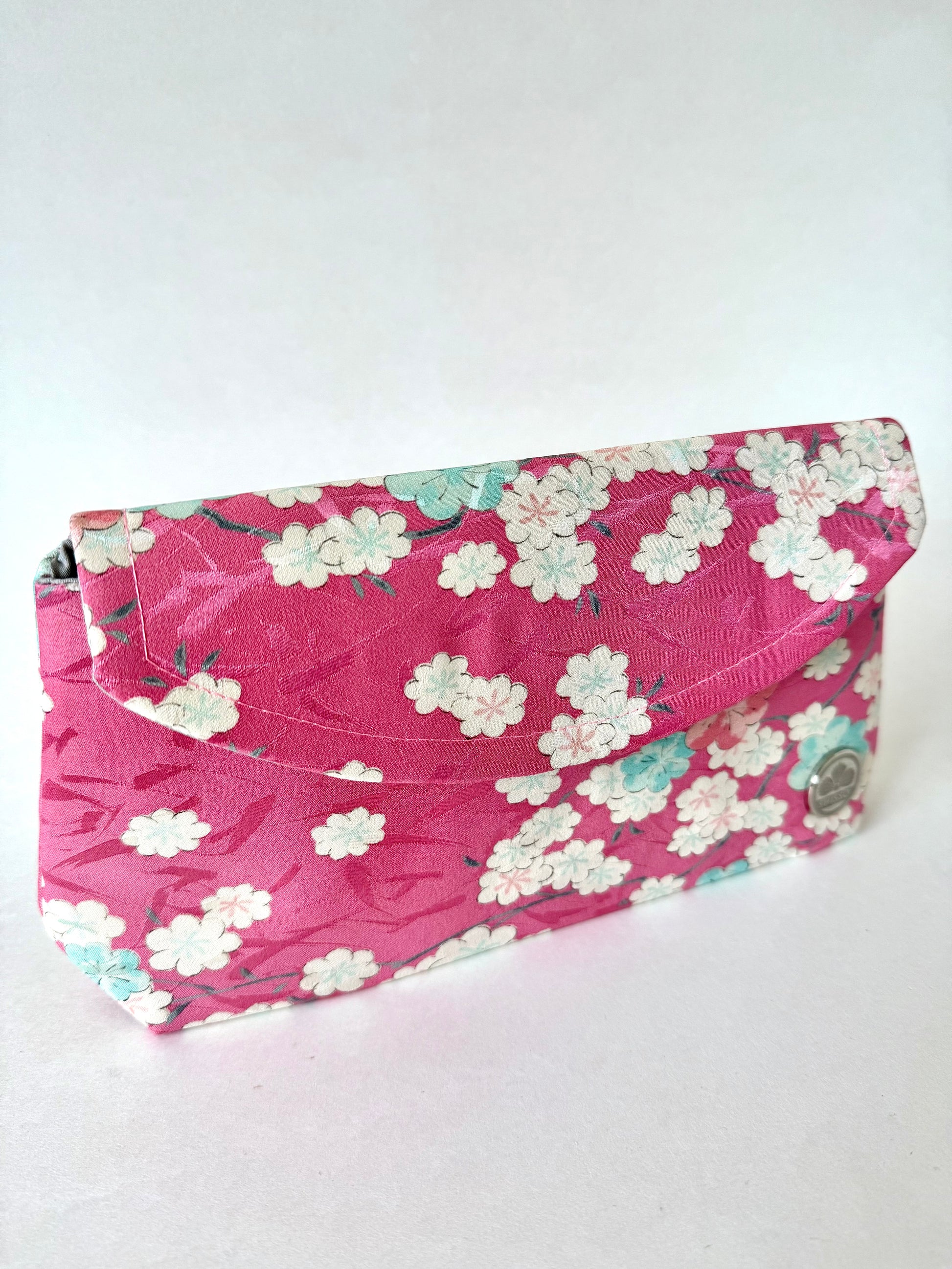 Angled view of pink kimono silk clutch showing subtle brushstroke pattern and fold-over design