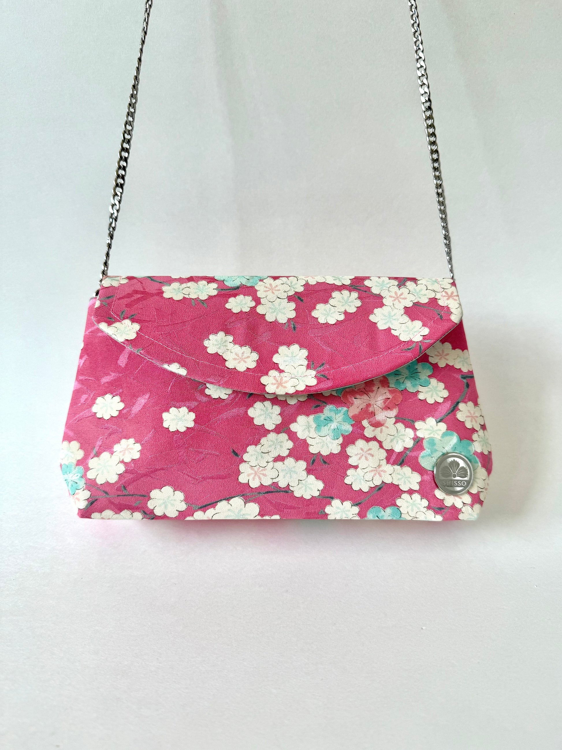 Pink kimono clutch handing from metal chain strap attached to hidden interior D-rings