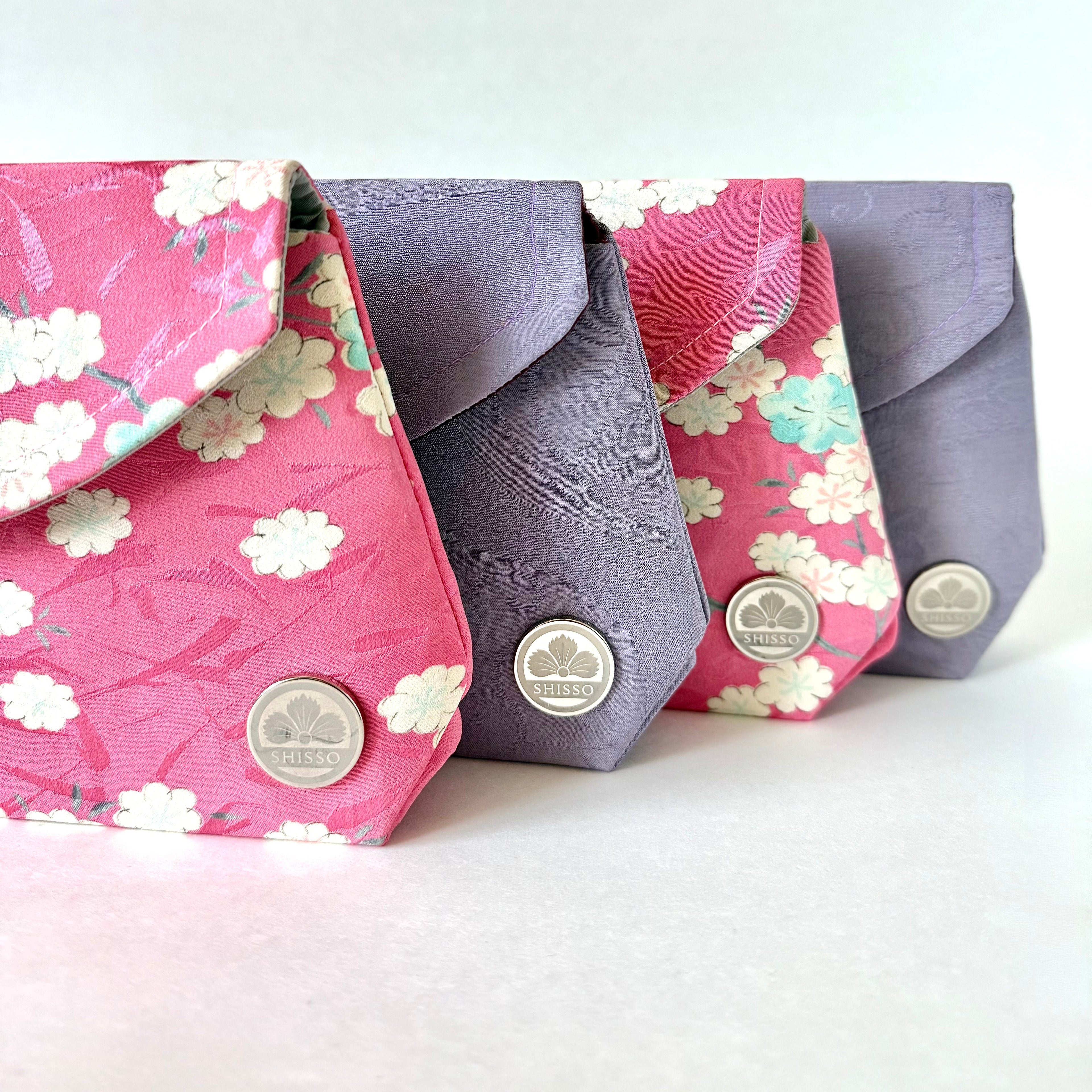 Four shisso clutches made from pink and purple kimono silk featuring cherry blossoms, streams, and other japanese motifs