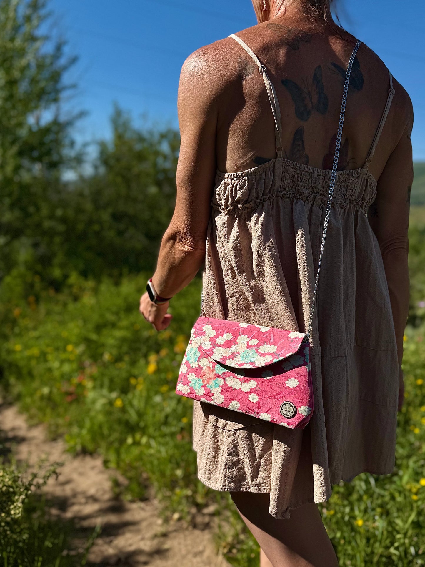 Fold-over pink kimono clutch shown from side while carried with chain strap outdoors