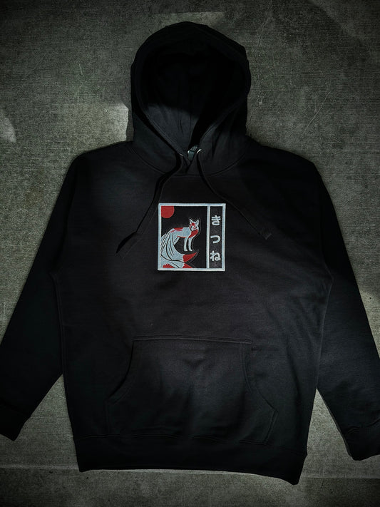 Flat lay of Kitsune embroidered hoodie on gray concrete background, showing black hoodie with minimalist white and red yokai embroidery on front.