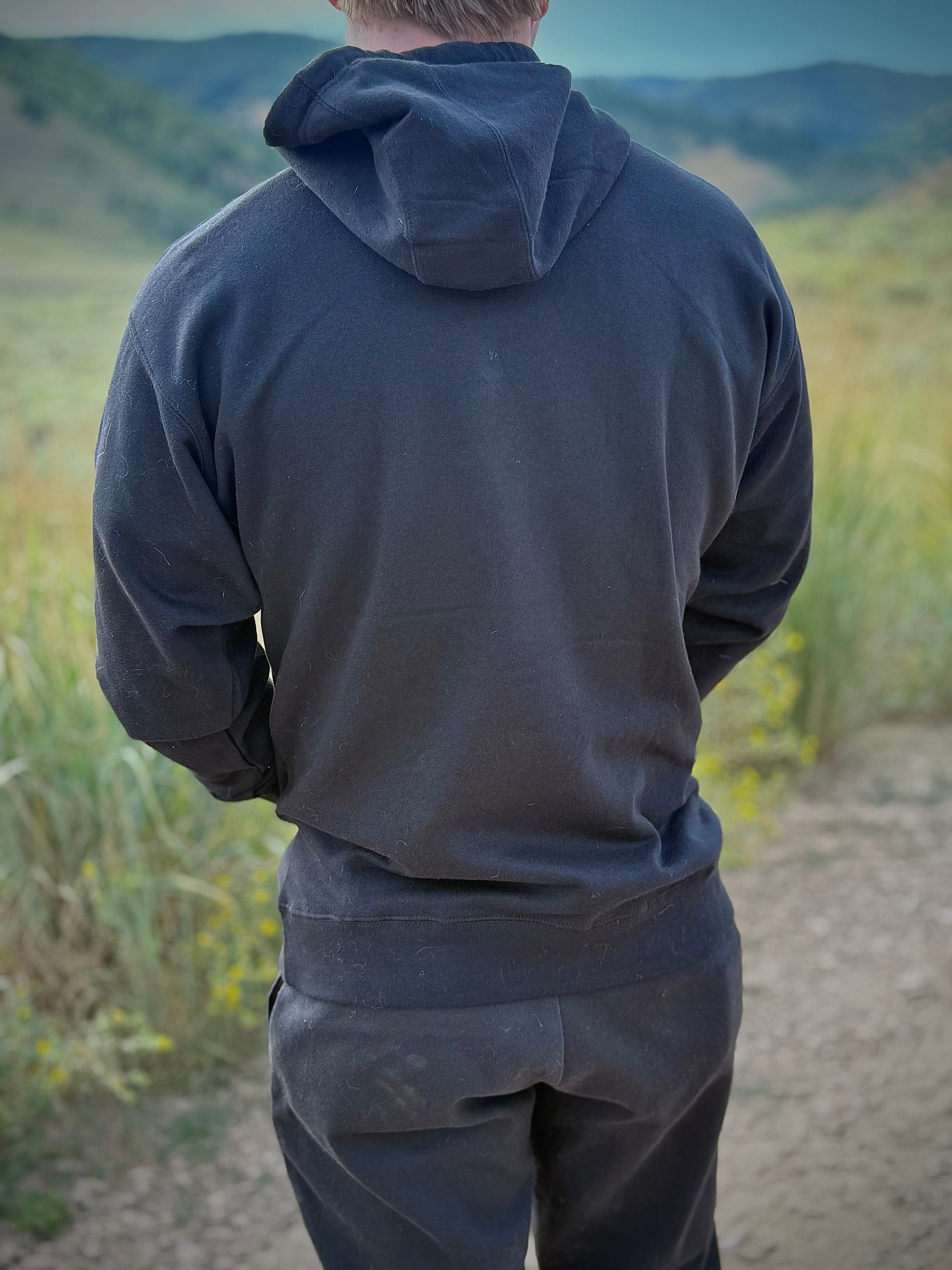 Back view of model wearing black Japanese design yokai hoodie in nature background, showing plain black fabric and clean minimalist design.