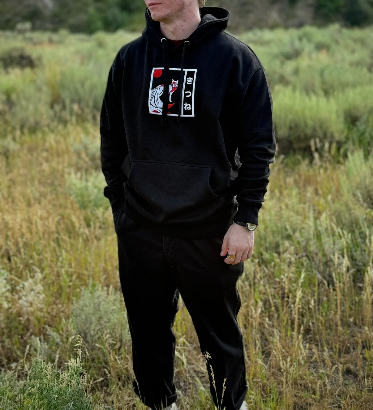 Person wearing black hoodie with embroidered Japanese Kitsune yokai design