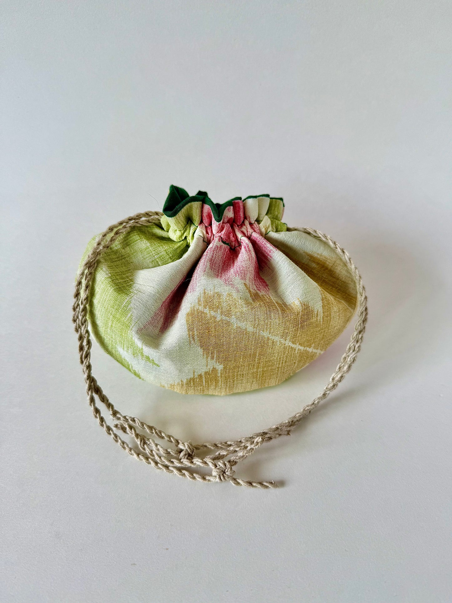 Backside view of beige kimono silk pouch featuring yellow, red, and green maple leaf motifs, cinched closed by hemp drawstrings