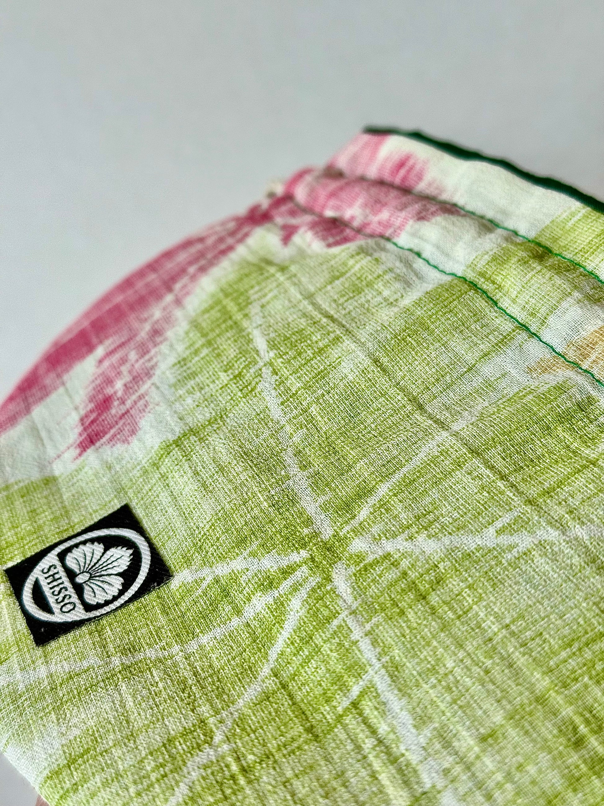 Front close up view of woven textured kimono silk featuring green and red maple leaf motifs in autumn hues