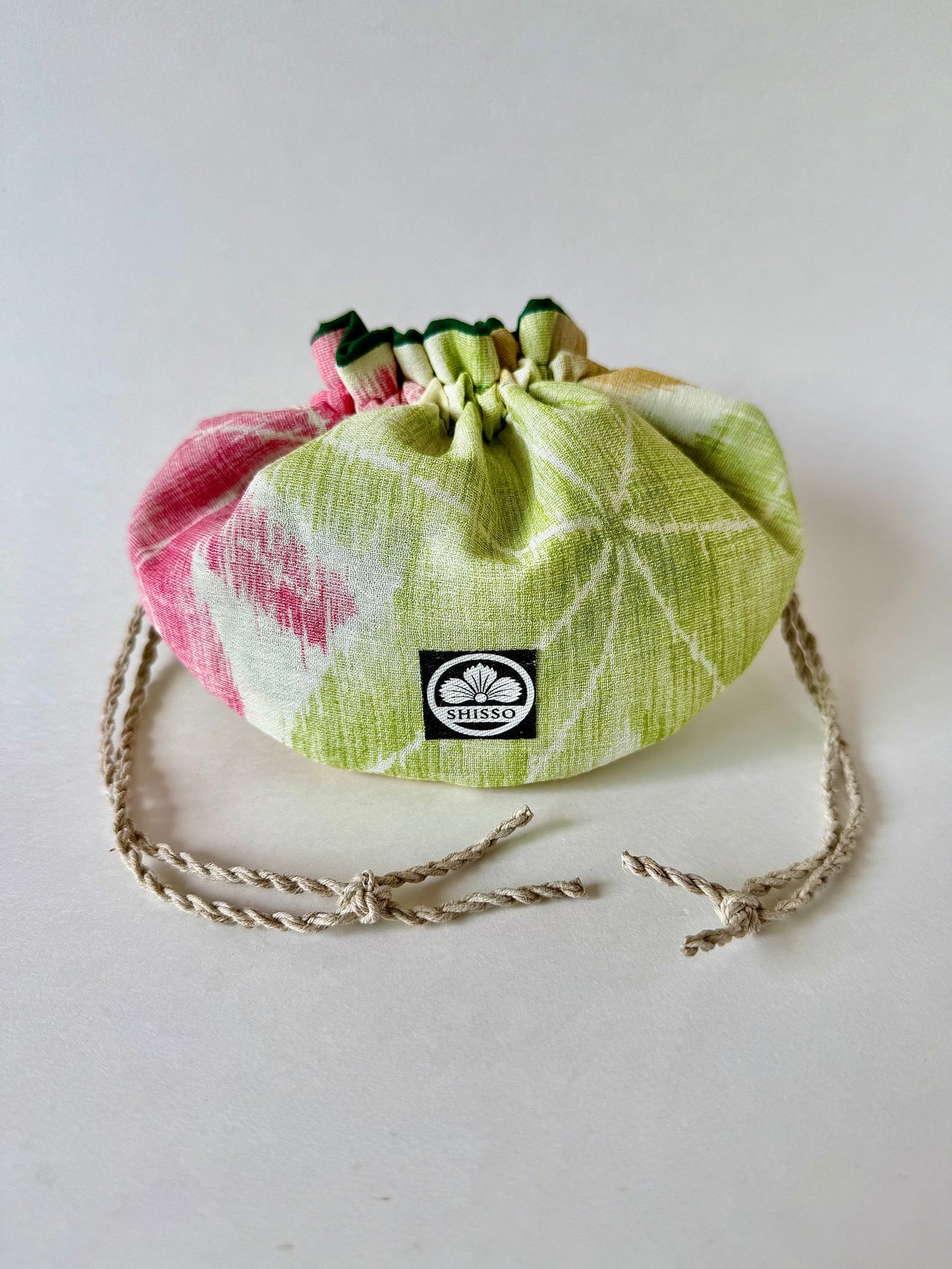 Front view of kimono silk pouch with green and red maple leaves pattern, cinched closed with natural hemp drawstrings