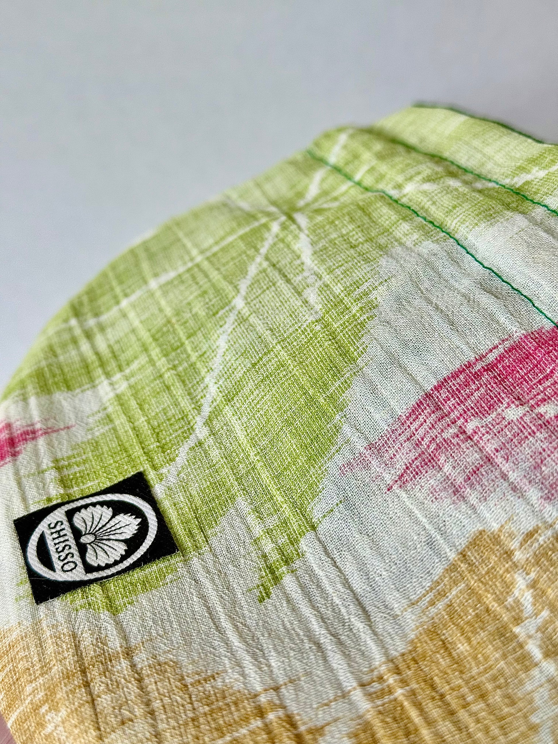 Close up of woven textured off white kimono silk with green, red, and yellow momiji pattern