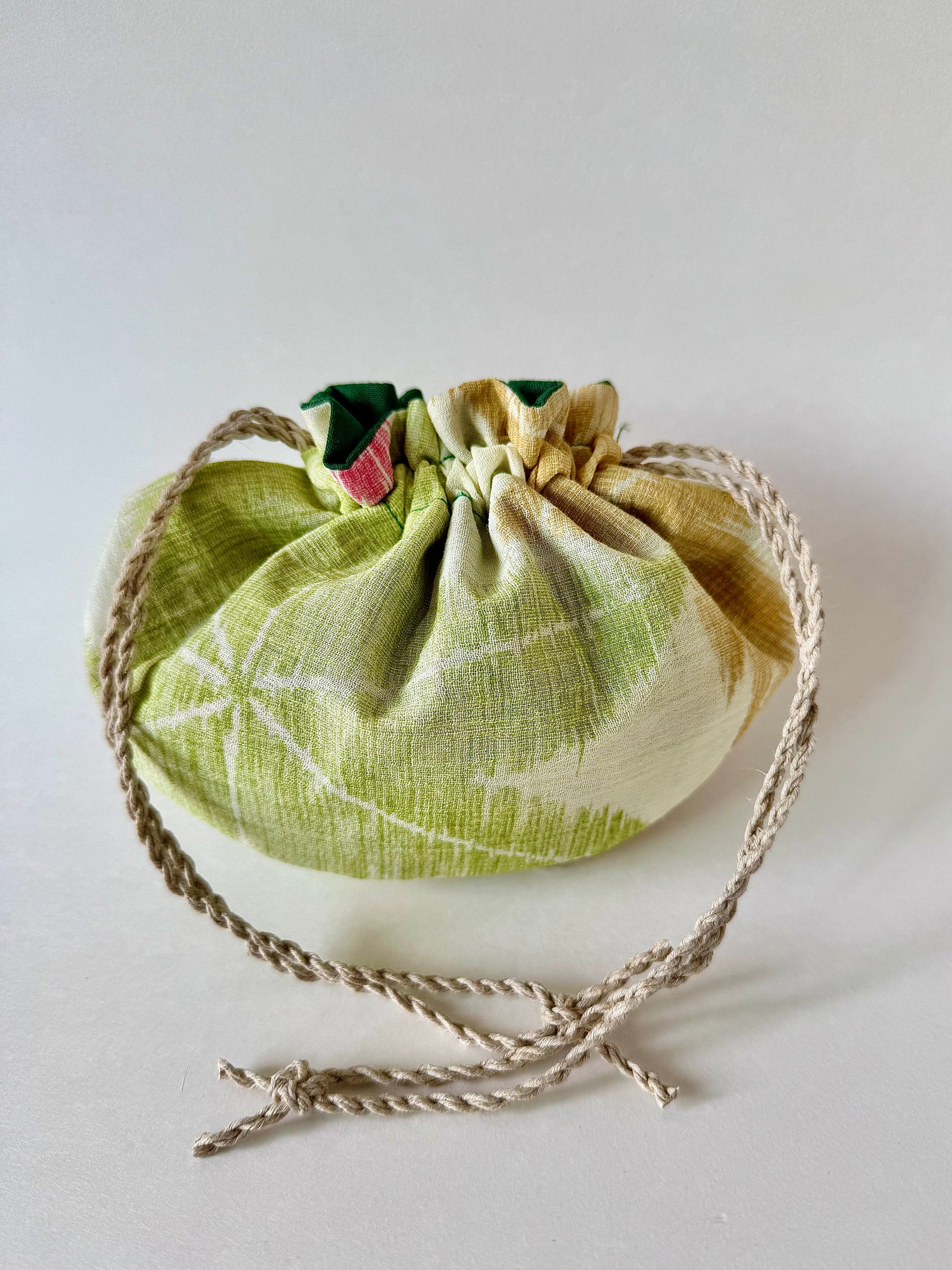 Back view of cinched closed off white kimono silk drawstring pouch with green, yellow, and red maple leaf pattern