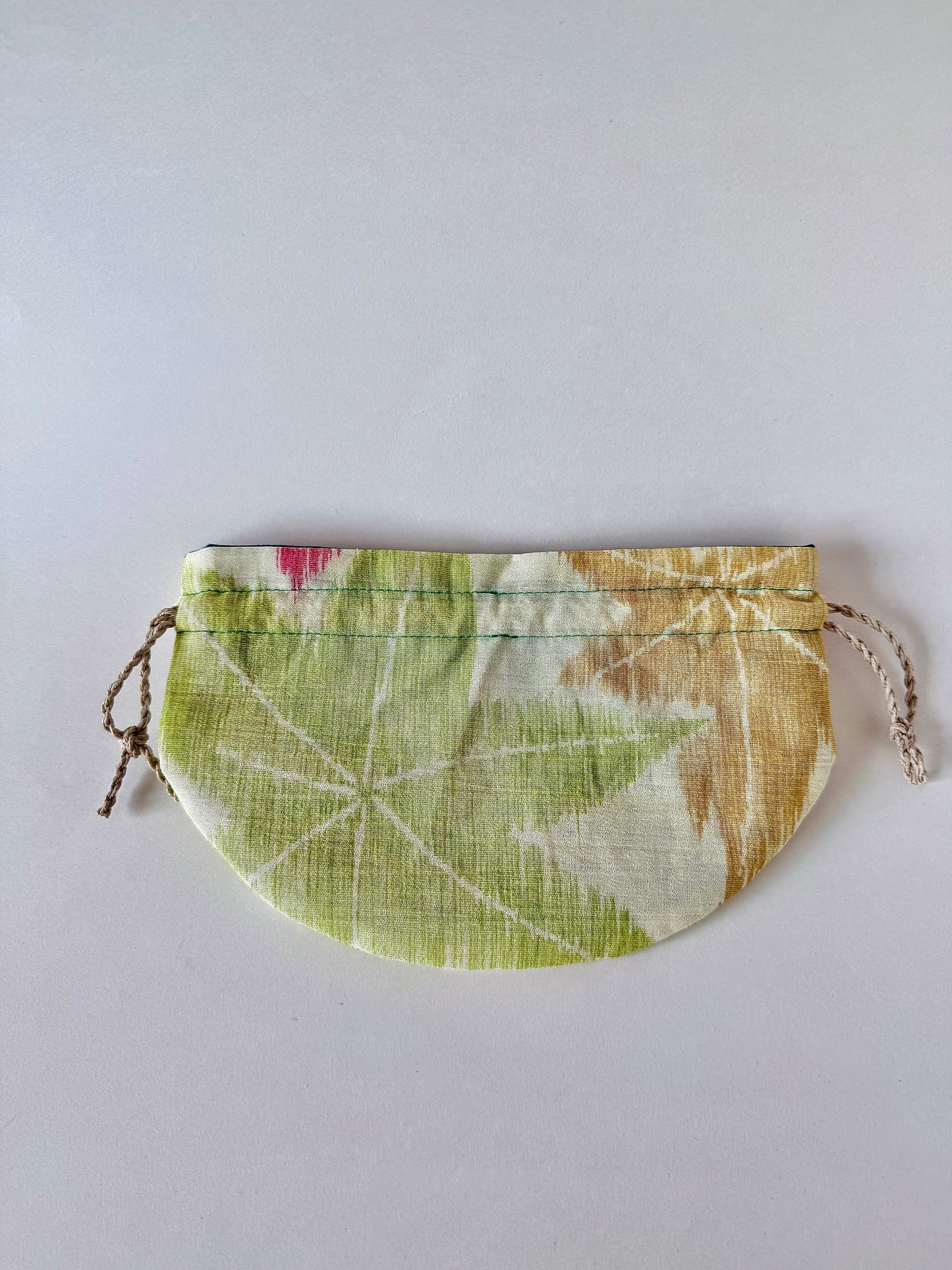 Backside of flat laying off white kimono silk drawstring pouch with green and yellow maple leaf design and slight red accent