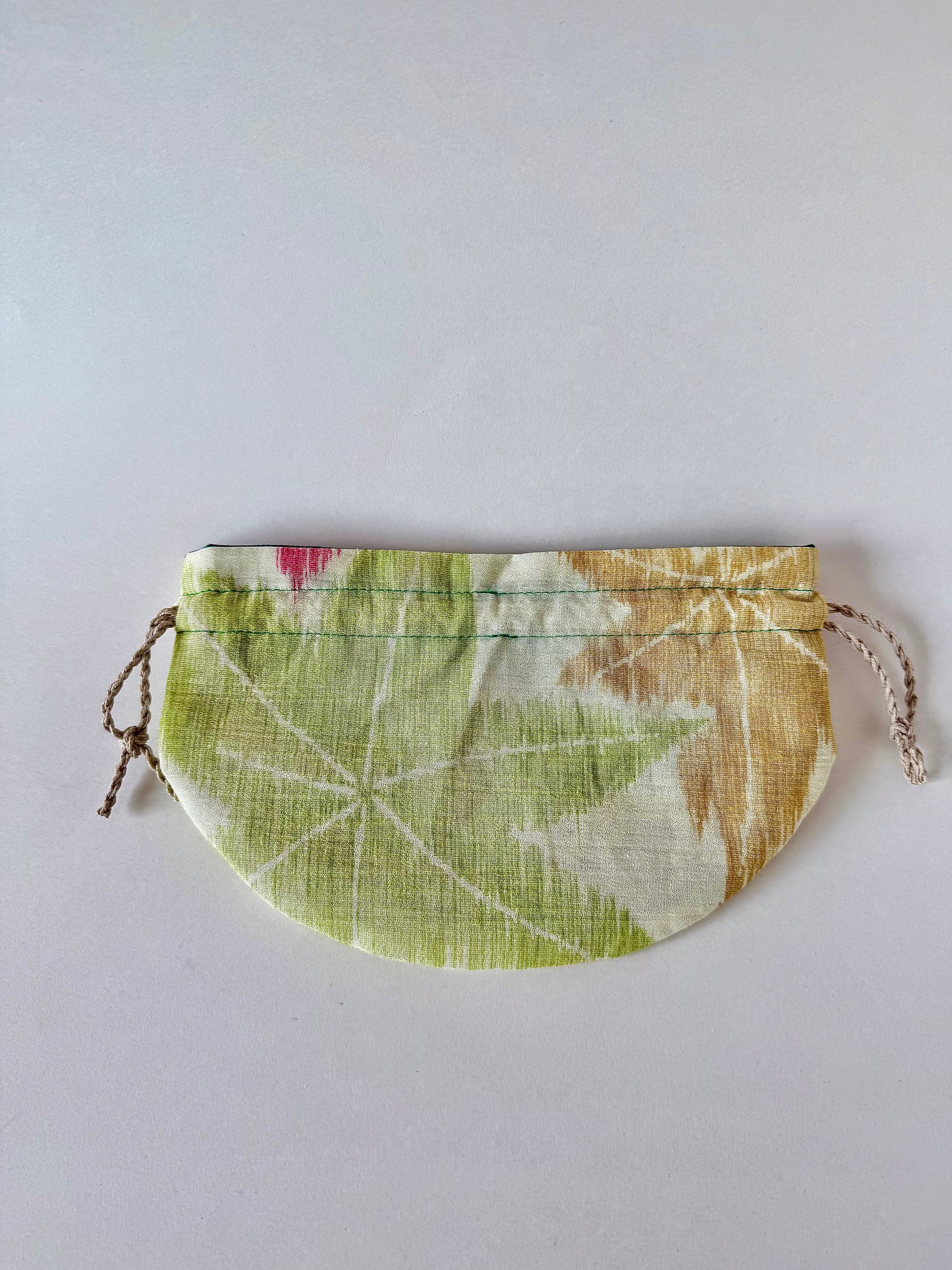Backside of flat laying off white kimono silk drawstring pouch with green and yellow maple leaf design and slight red accent