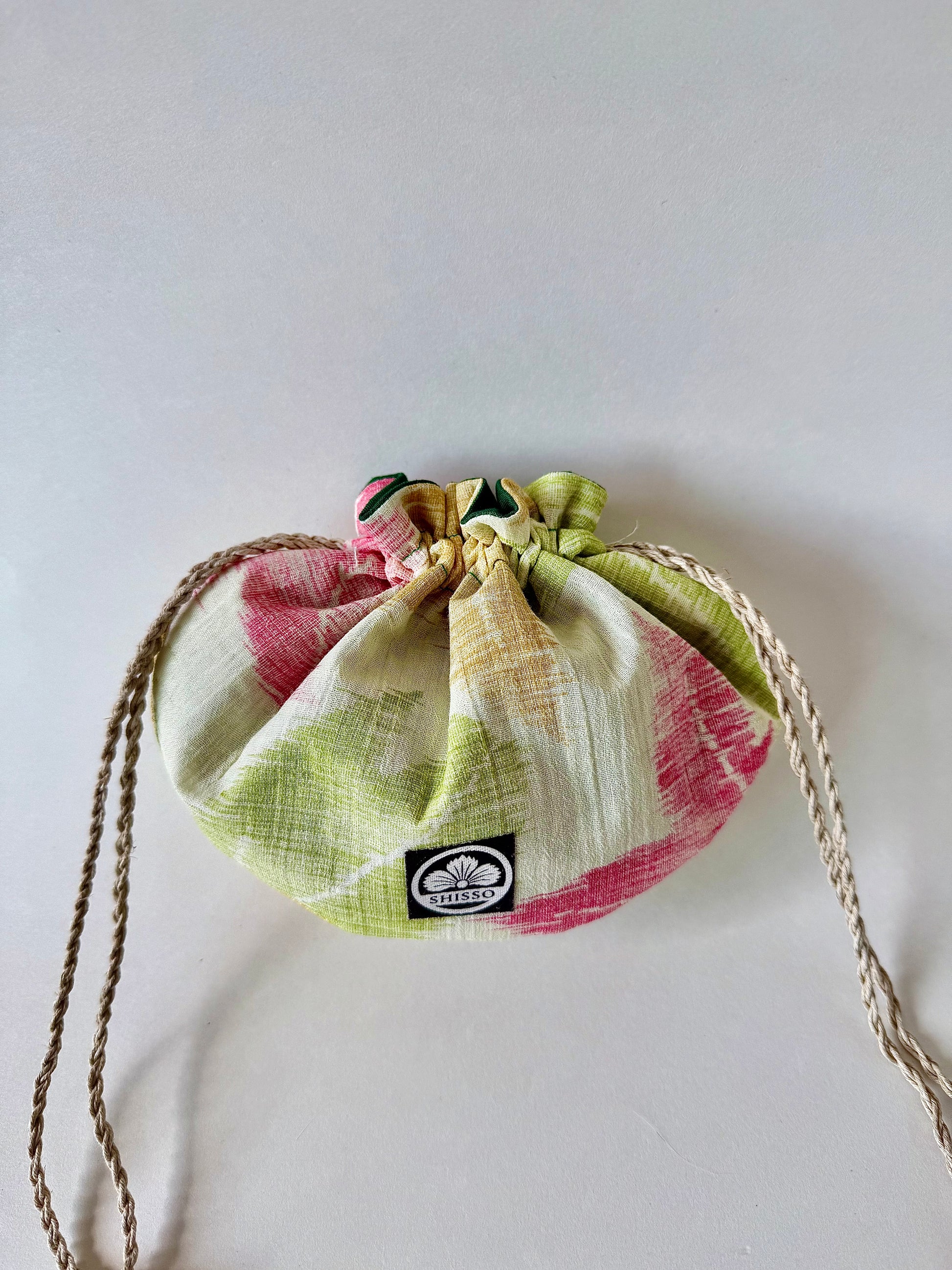 Front view of beige kimono sha silk pouch with autumnal red, green, and yellow Japanese maple leaf designs, cinched closed with natural hemp drawstrings