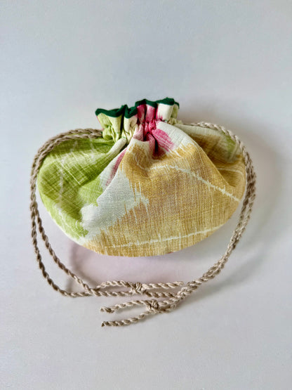 Back view of cinched closed beige kimono sha silk pouch featuring red, green, and yellow momiji motifs and natural hemp drawstrings