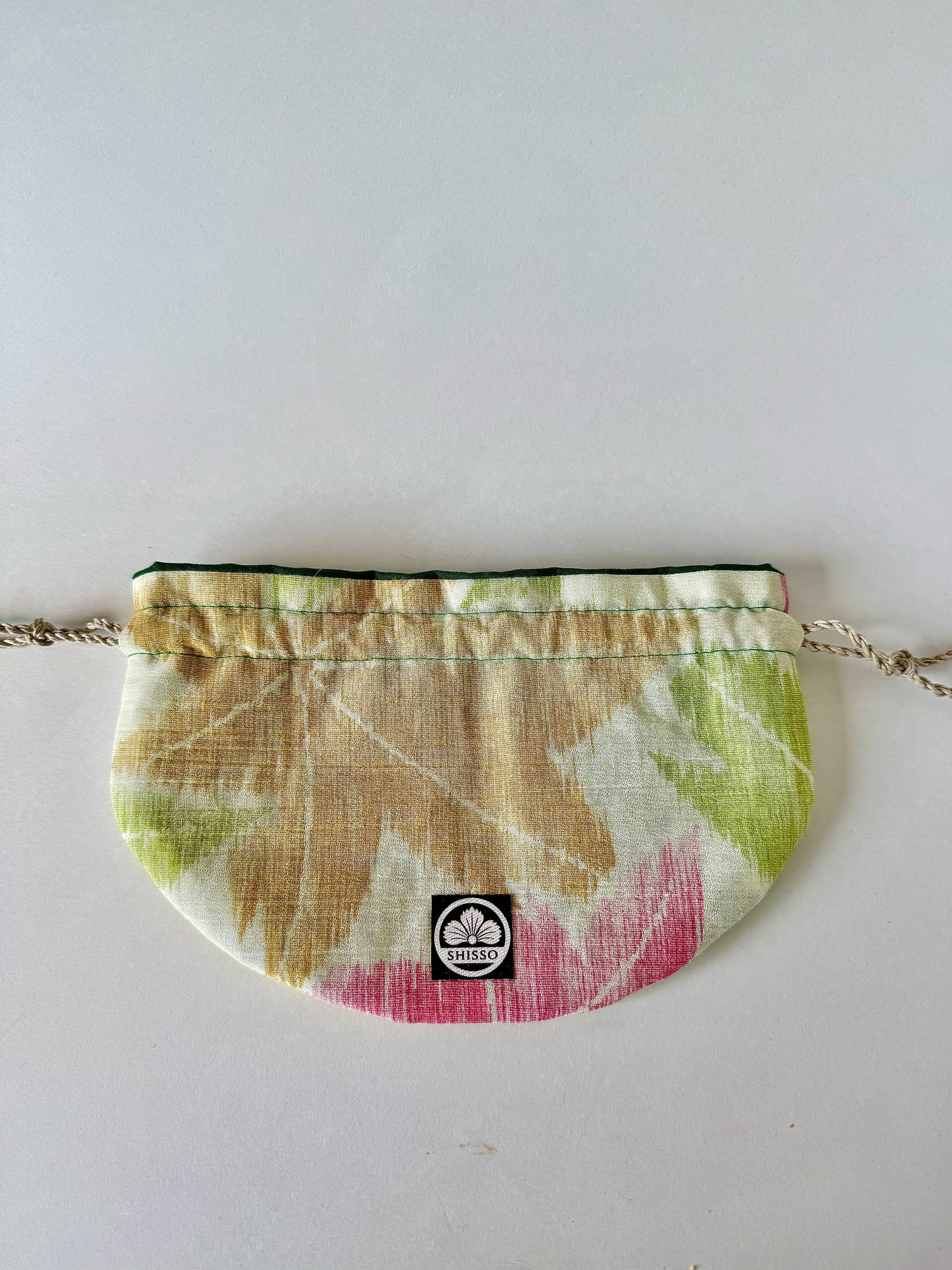 Flat laying beige woven kimono sha silk drawstring pouch featuring red, green, and red momiji motifs in autumn hues