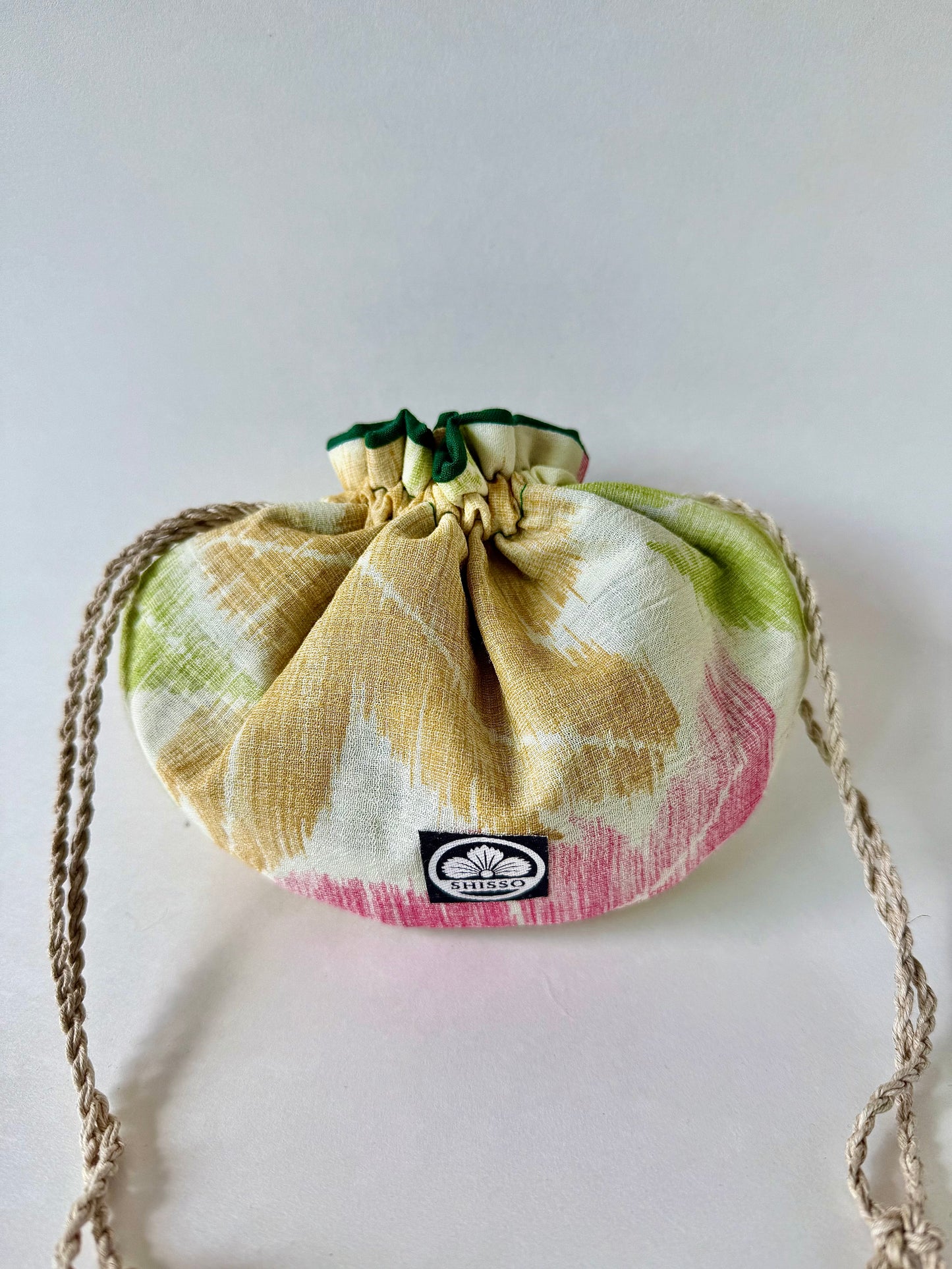 Front view of cinched closed off white woven kimono sha silk drawstring pouch featuring red, green, and red momiji motifs in autumnal hues