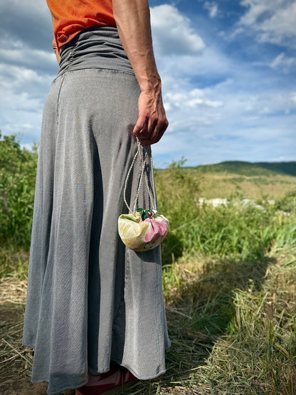 Small beige woven kimono silk pouch featuring red, yellow, and green Japanese maple leaf designs being held in hand by hemp drawstrings in nature