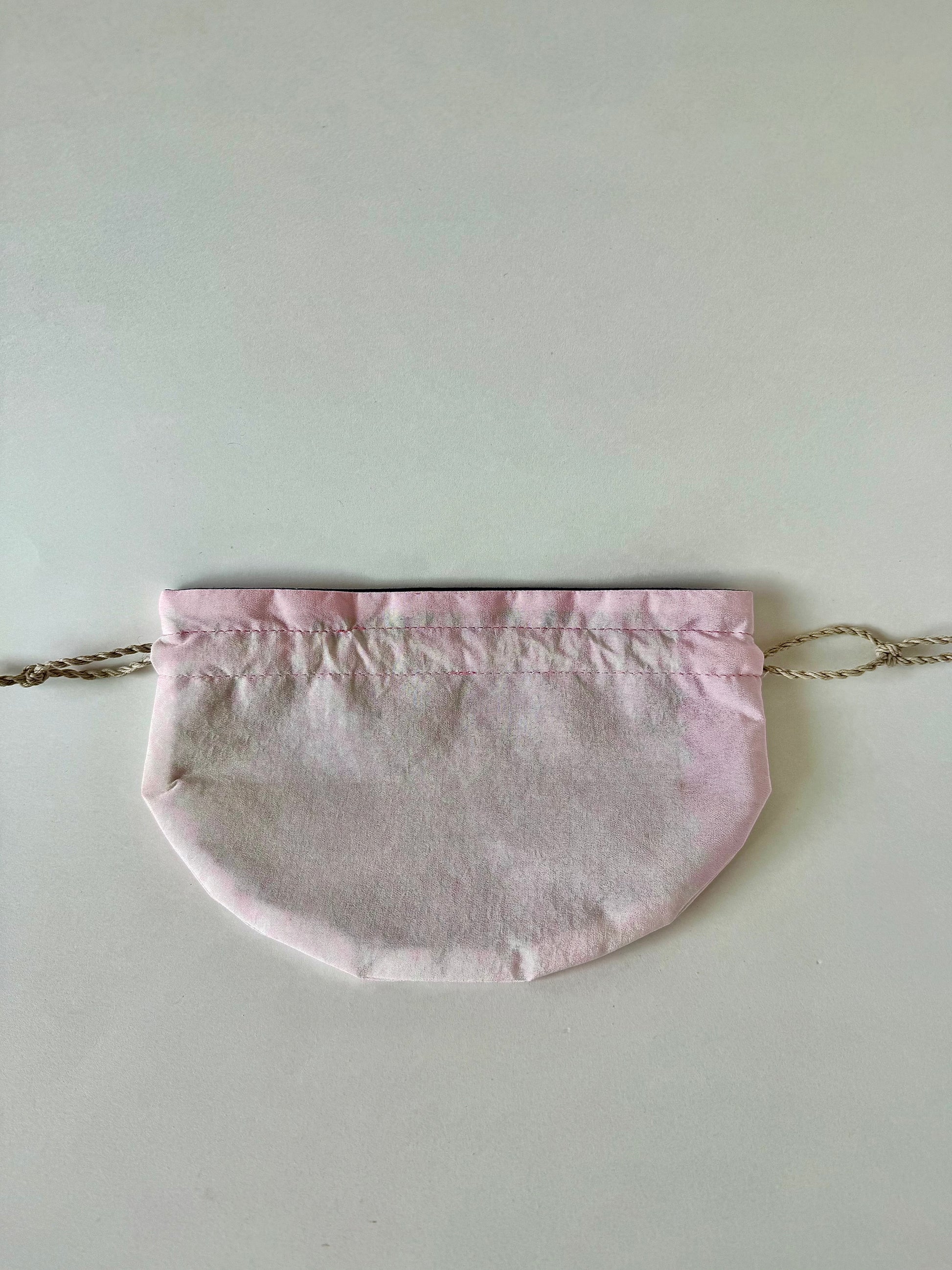 Backside view of flat laying pink kimono silk drawstring pouch with slightly darker pink accents and patterns