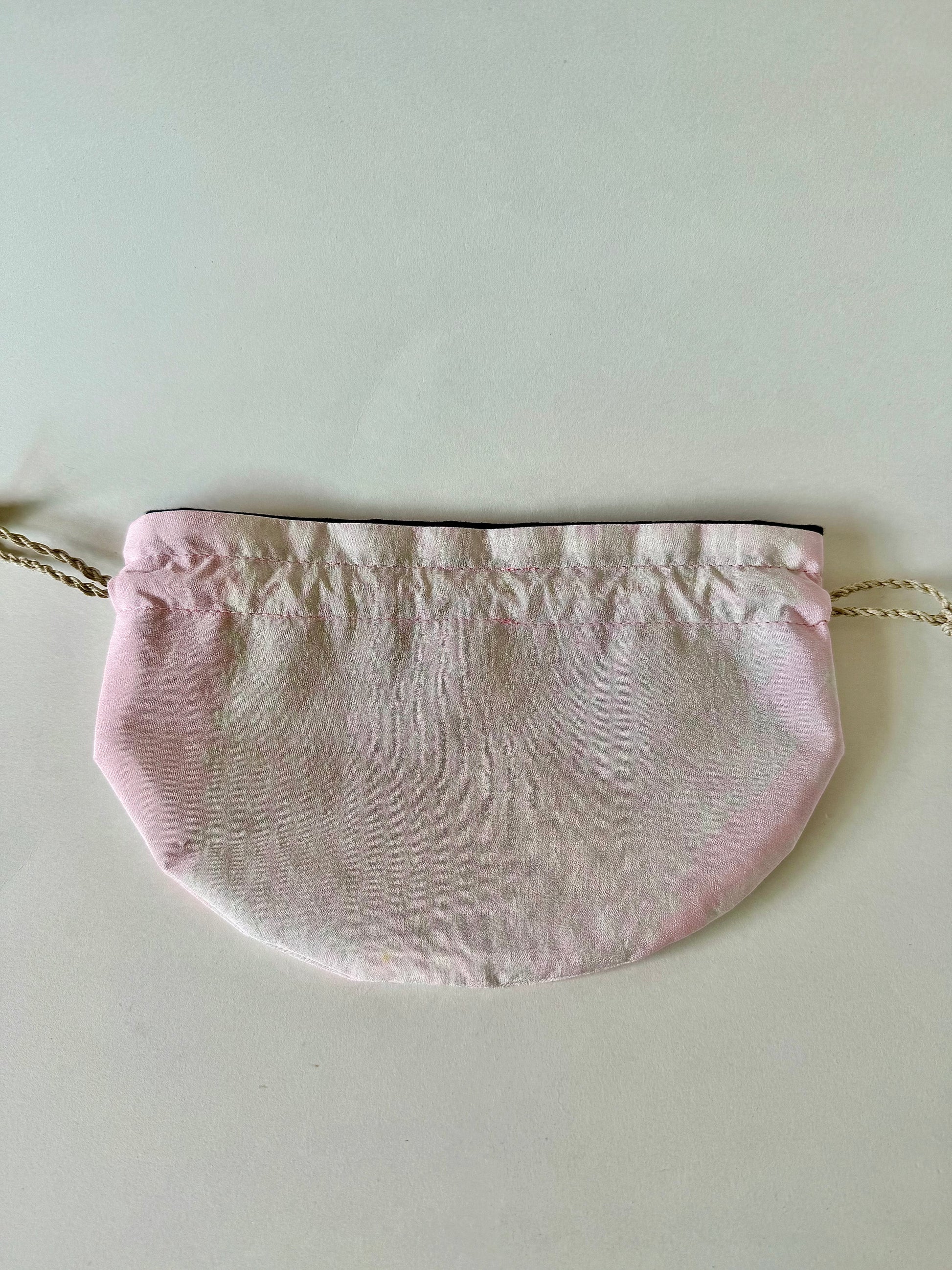 Backside of pink kimono silk drawstring bag laying flat with darker pink edges and natural hemp cords