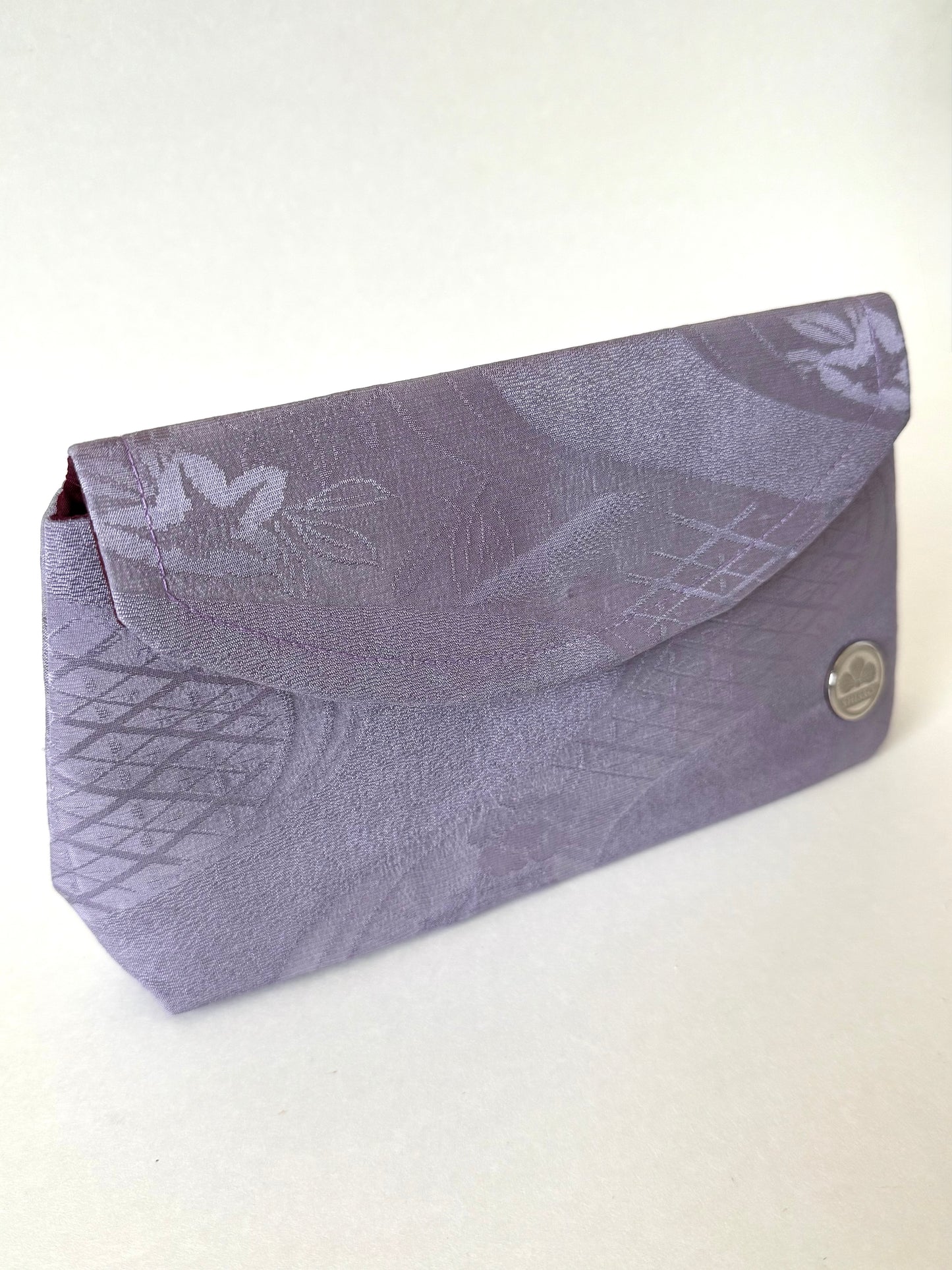 Front angled view of purple kimono silk clutch bag with streams and geometrical patterns