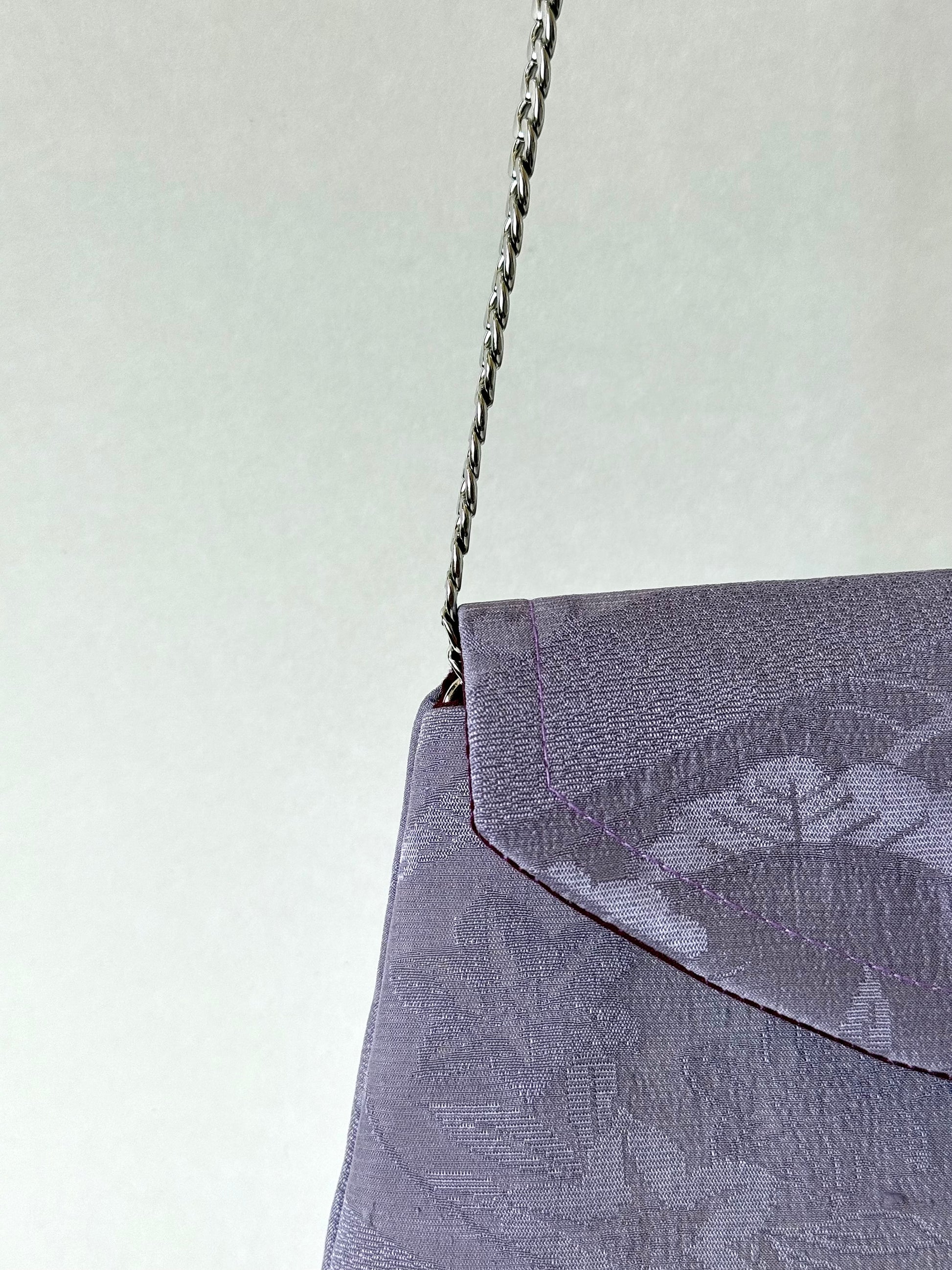 Close up of silver metal chain strap entering the interior of purple kimono silk clutch