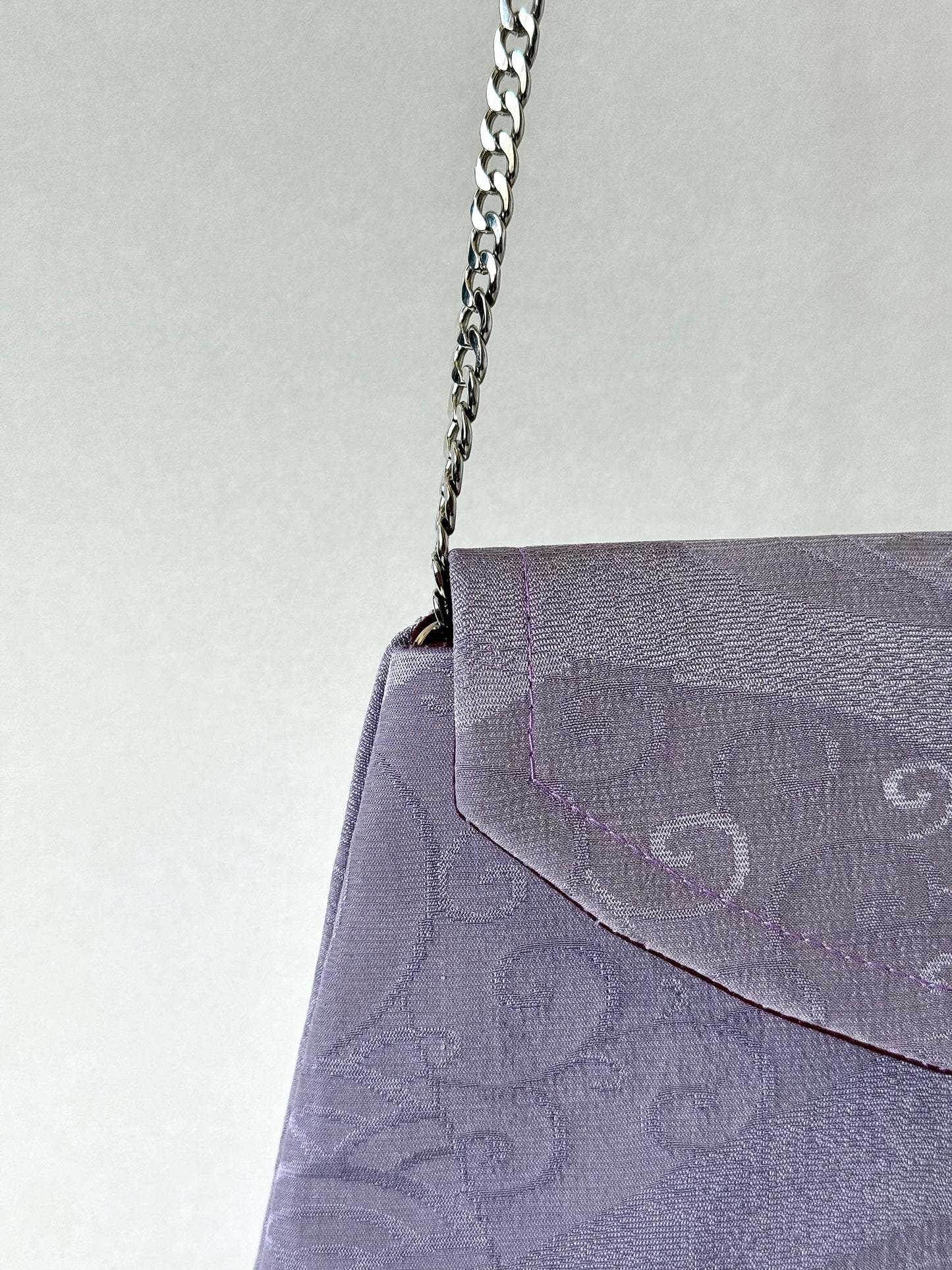 Close up view of metal chain link strap attached to purple kimono silk clutch