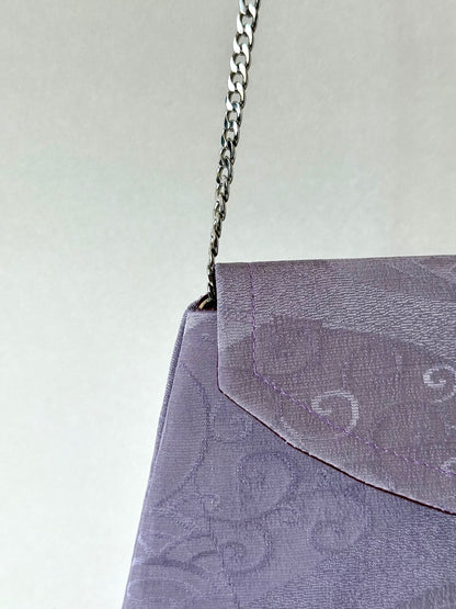 Close up view of metal chain link strap attached to purple kimono silk clutch