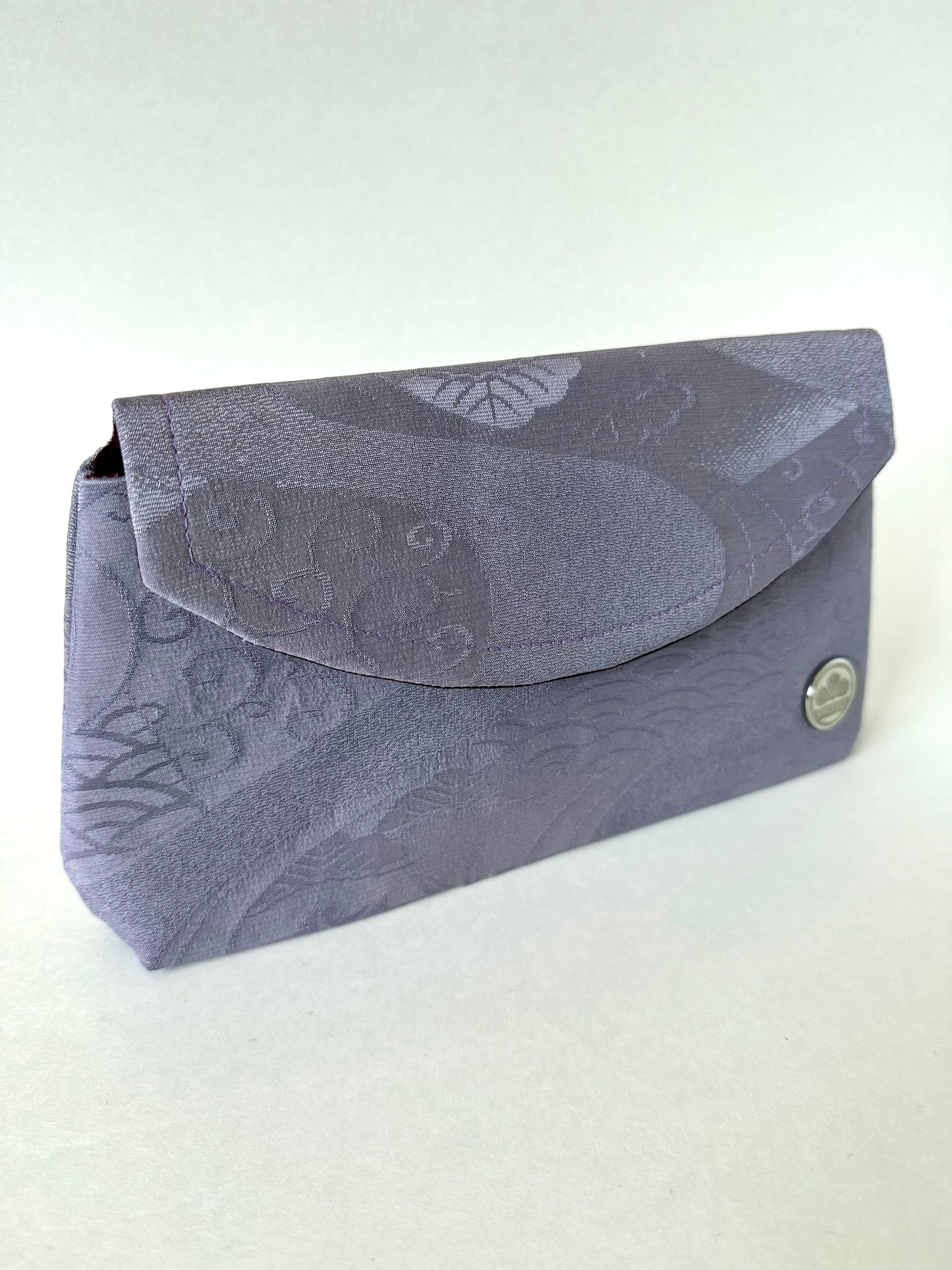 Front left angle of purple chirimen silk clutch with wagara, floral, and flowing stream motifs