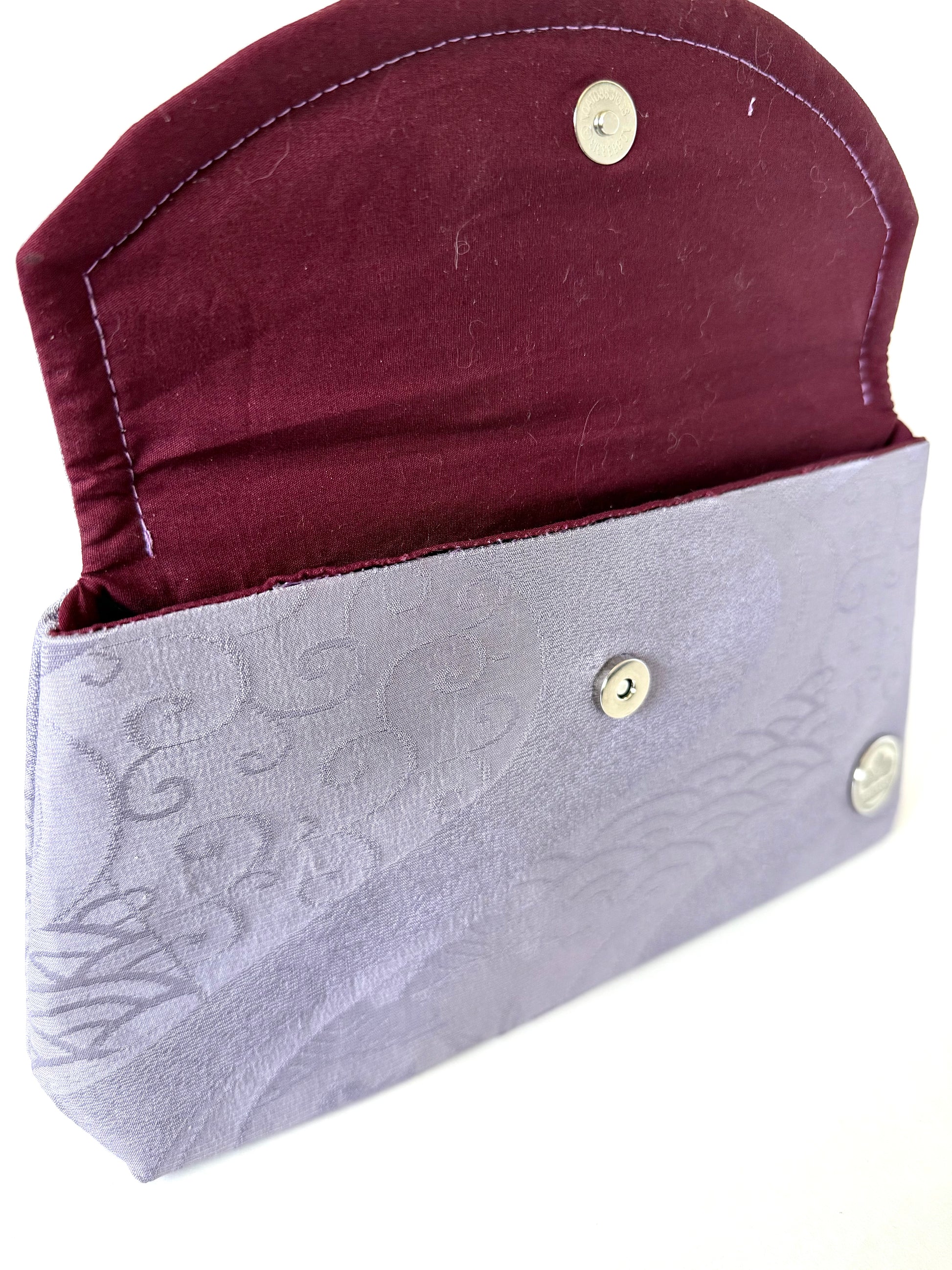 Front view of opened clutch flap showing hand stitching, magnetic closure, and purple topstitching on wine colored cotton interior