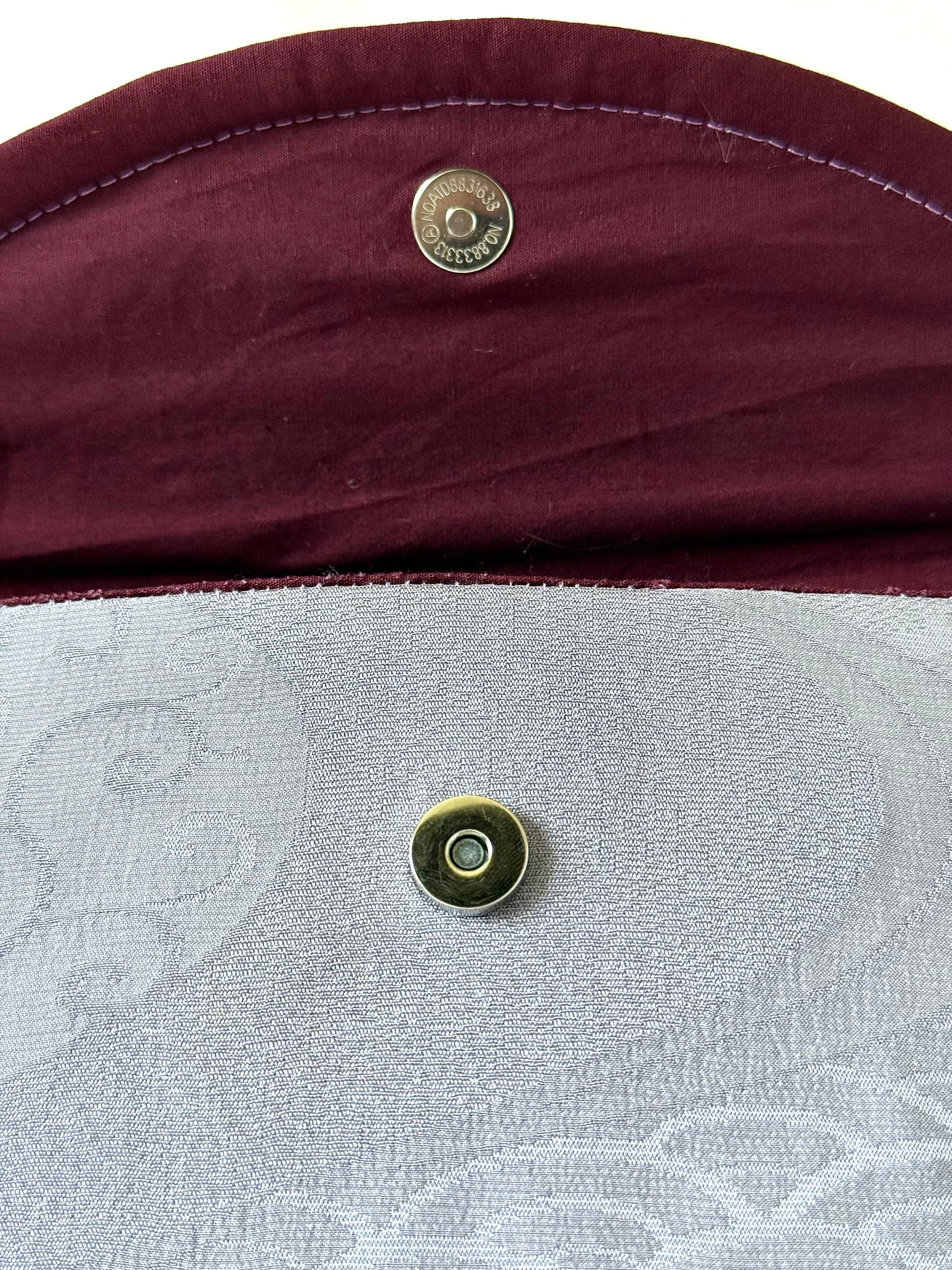 Close up of magnetic closure on main body and wine colored cotton broadcloth interior with purple top stitching
