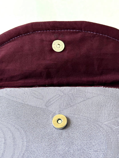 Close up of silver colored magnetic closure on wine colored cotton interior of top flat and main body of purple silk clutch 